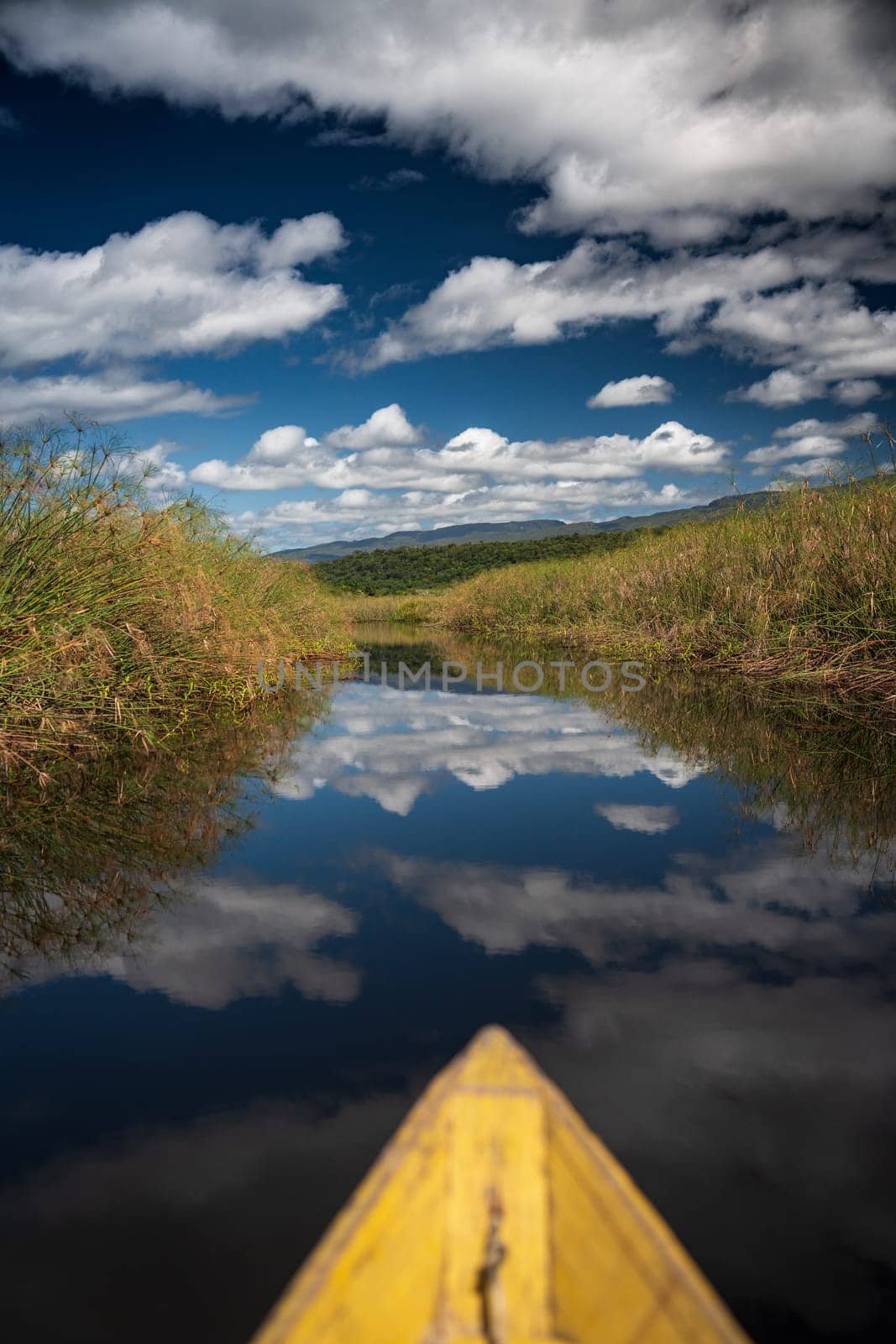 Wooden Canoe Navigating a Narrow Canal Reflecting Blue Sky by FerradalFCG