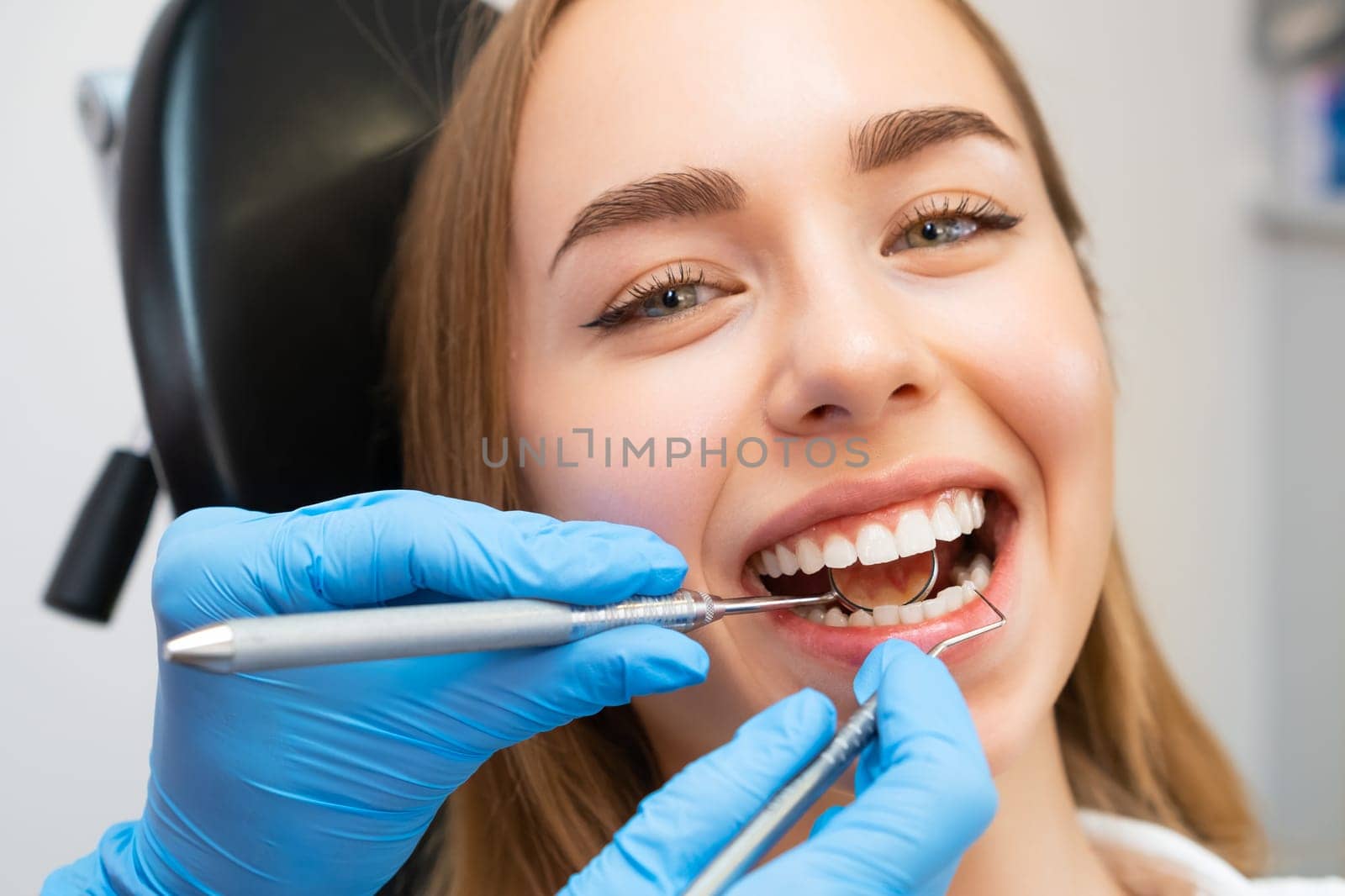 Female patient sitting in chair during dental treatment at dentist office. Doctor checks front teeth using instruments to check teeth strength