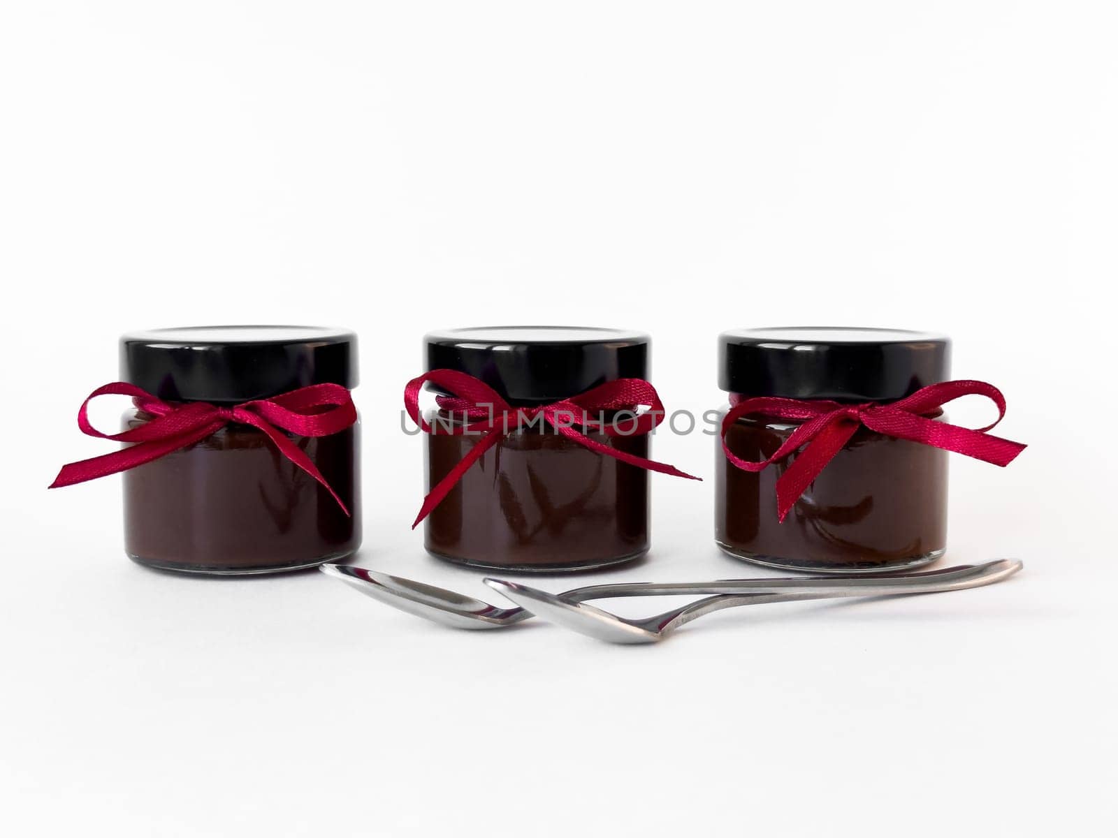Elegant chocolate jars with red ribbons and silver spoons on white background.