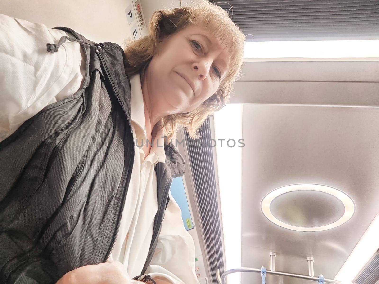 Blonde adult enjoys her excursion by capturing a selfie while traveling on a train, showcasing her blogging lifestyle.