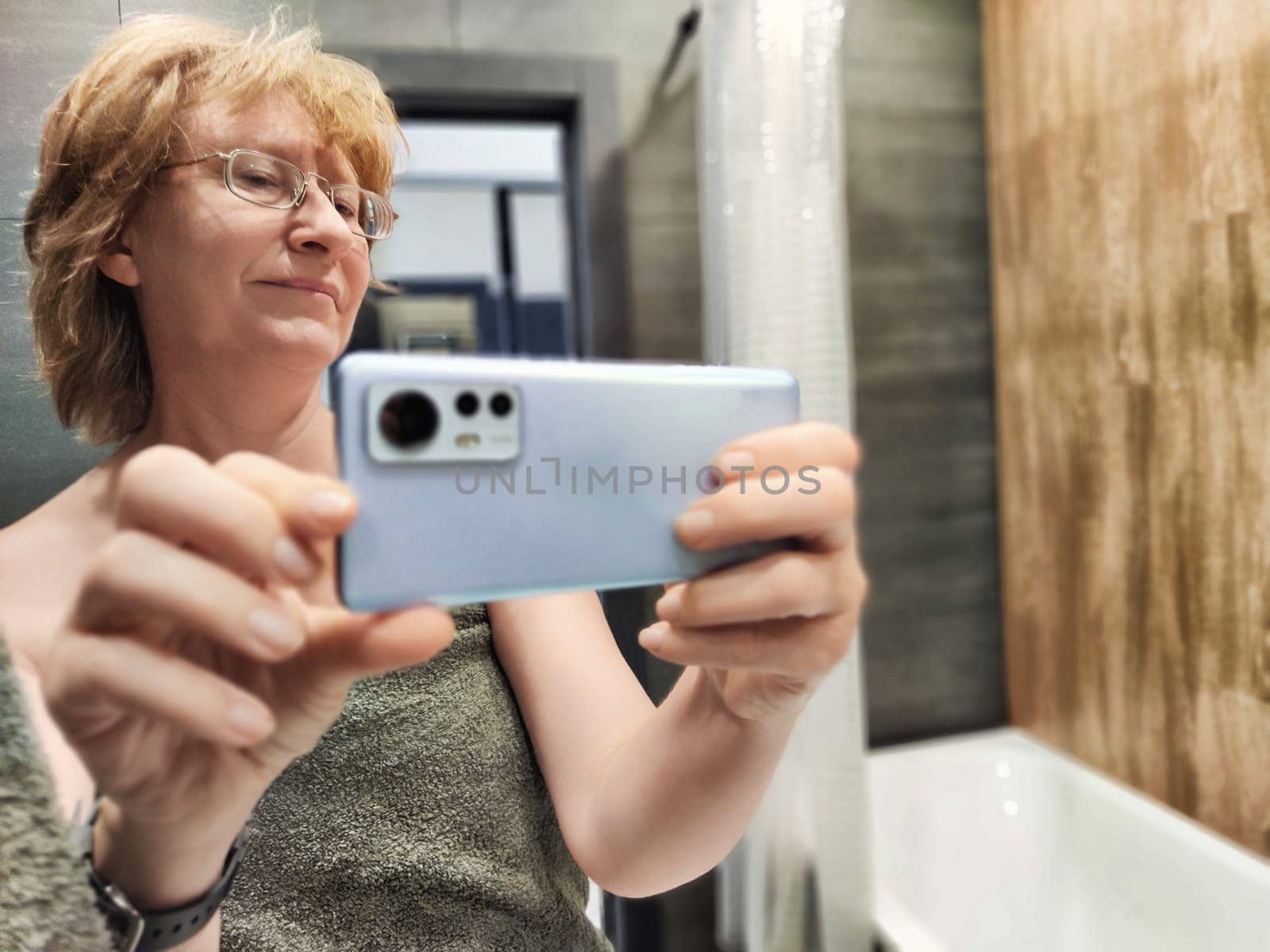A middle-aged woman captures a candid selfie in her bathroom right after waking up, portraying a relaxed morning vibe.