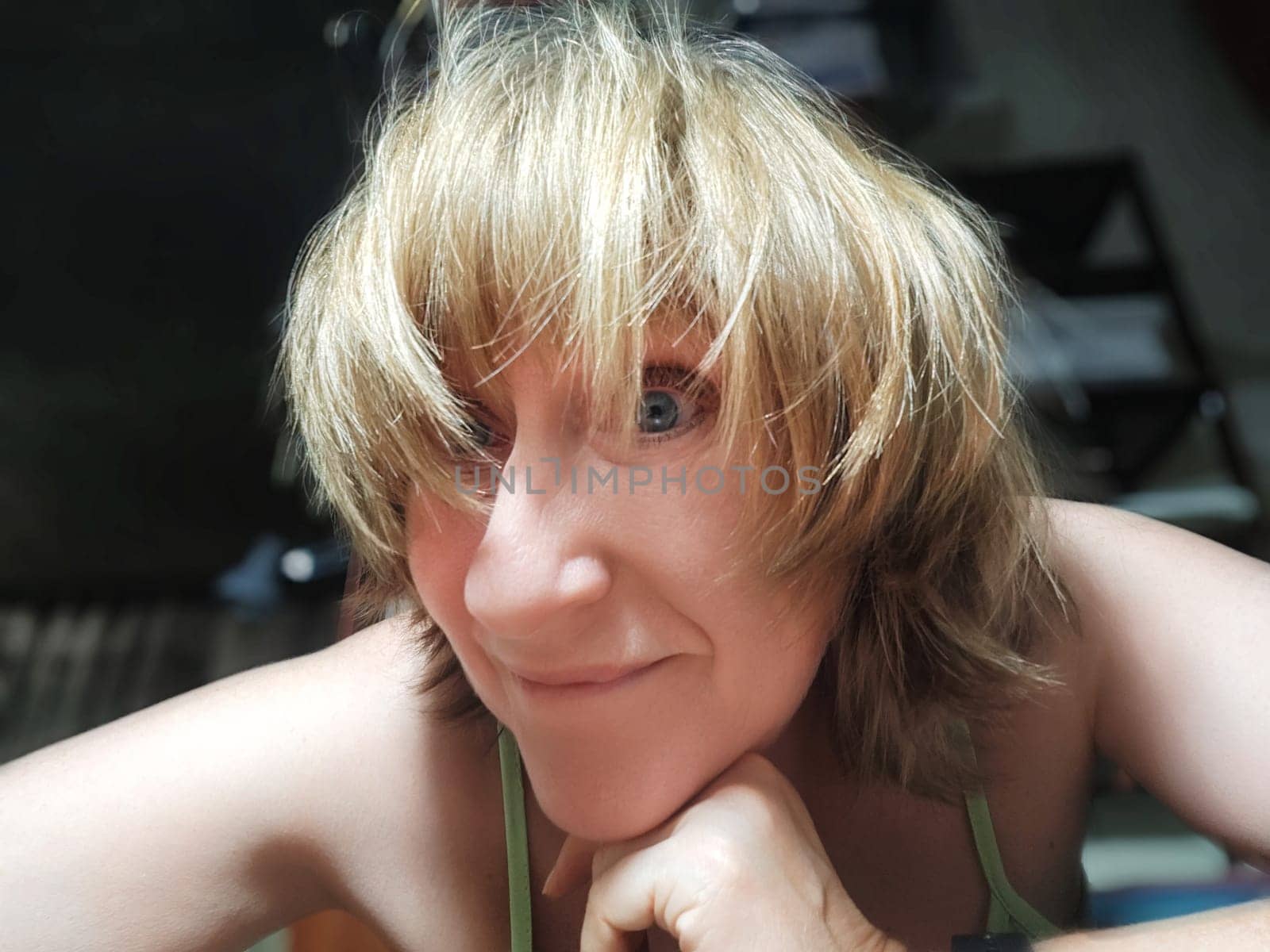 Energetic middle aged woman with blonde hair smiles and takes a playful selfie in a casual indoor setting