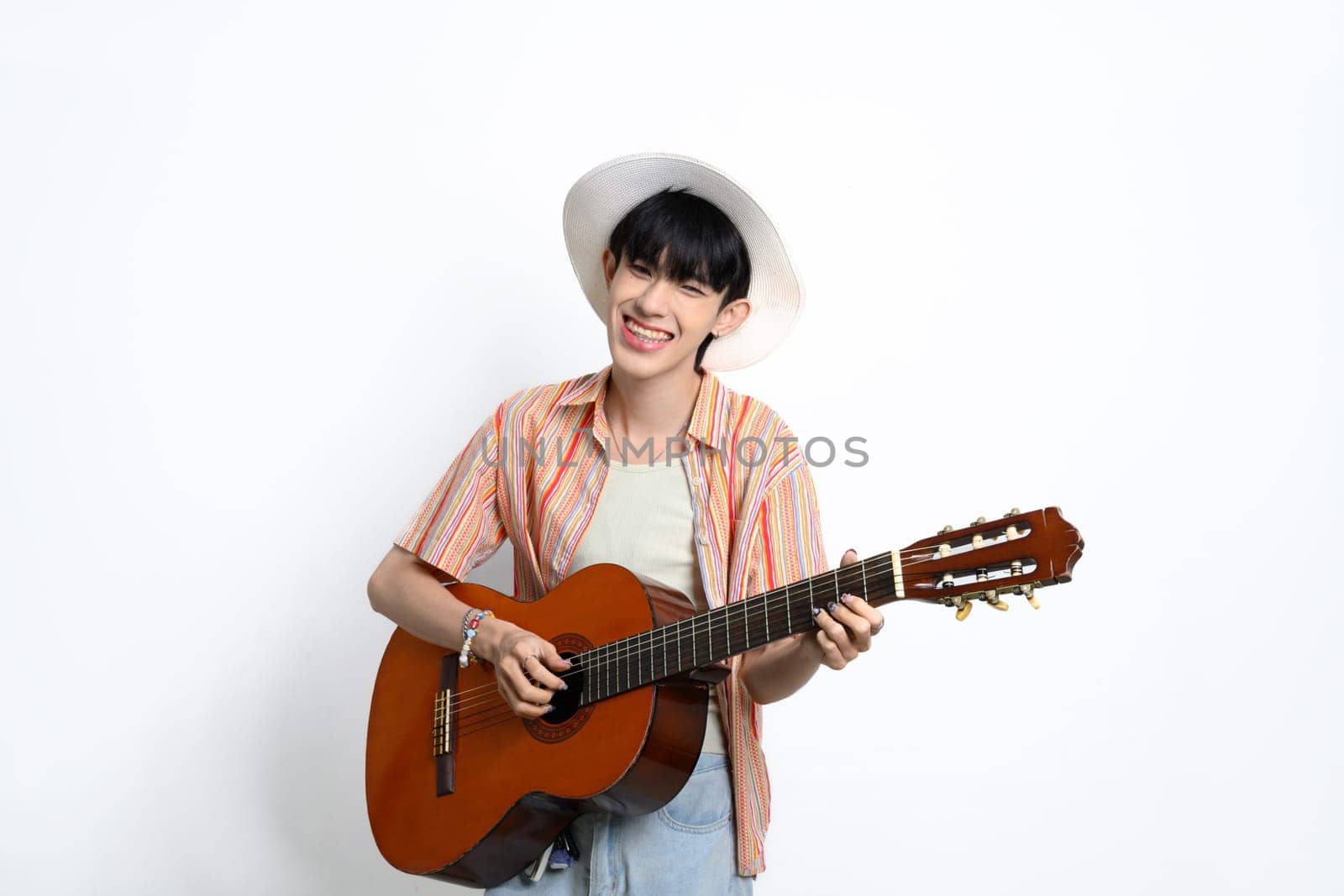 Pretty asian man wearing a straw hat holding a guitar against white background.