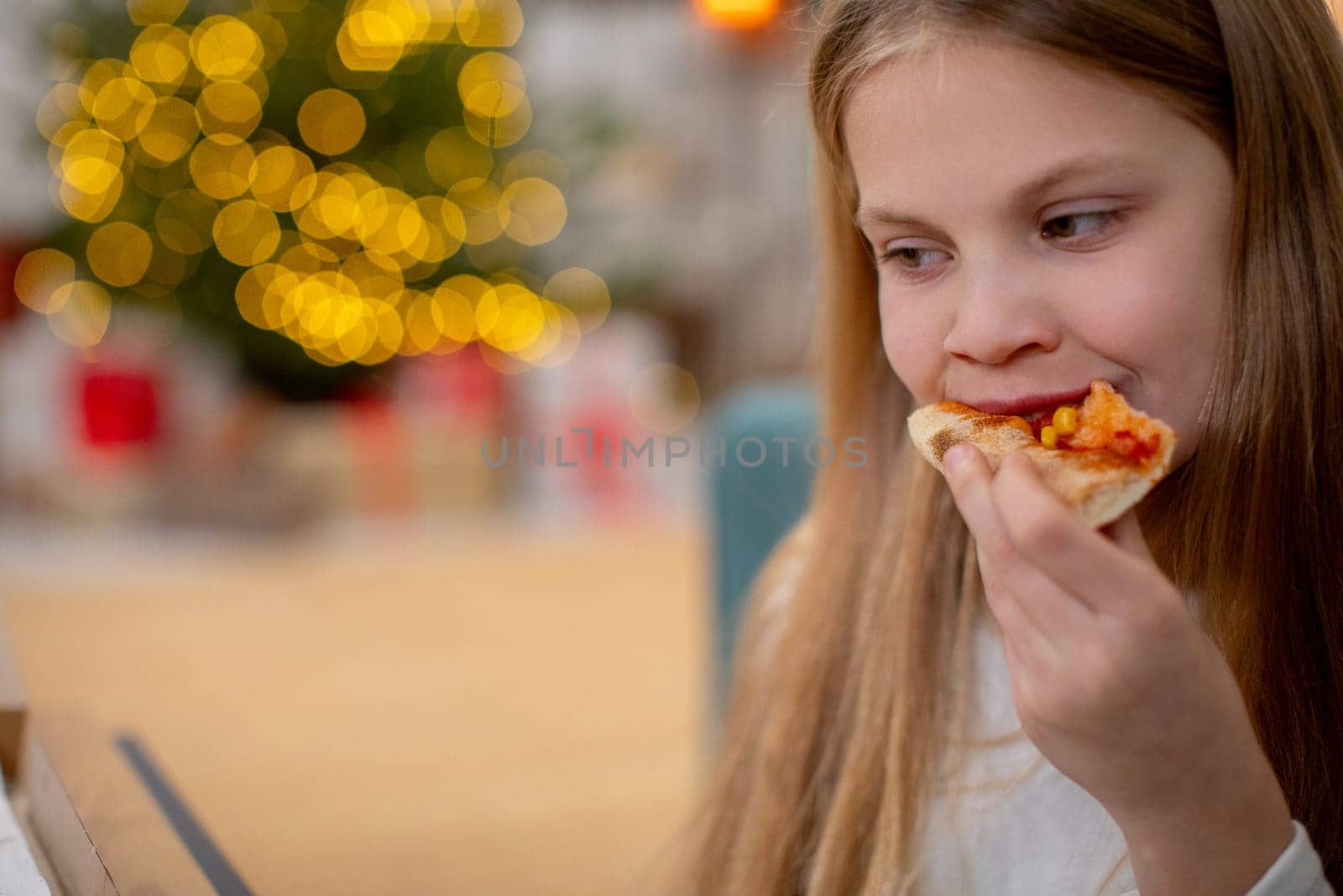 A young girl is taking delight in enjoying a slice of delicious pizza while surrounded by a joyful holiday atmosphere