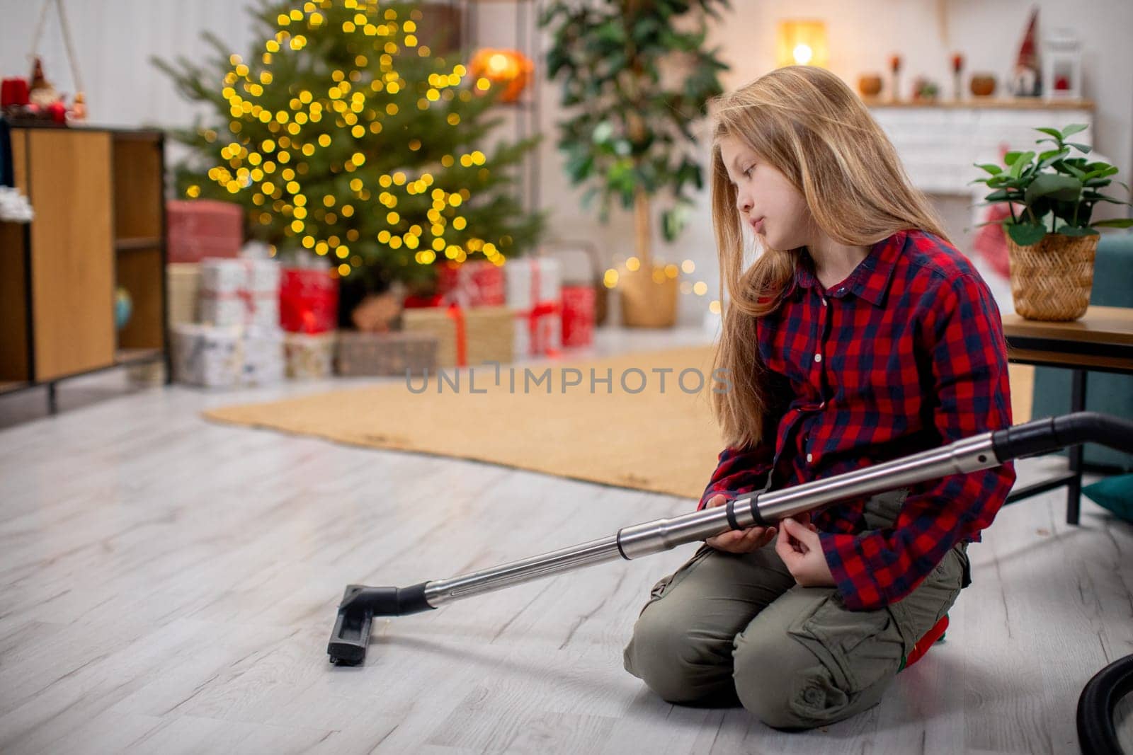 A person vacuums a festive room with a decorated Christmas tree, creating a cozy holiday atmosphere