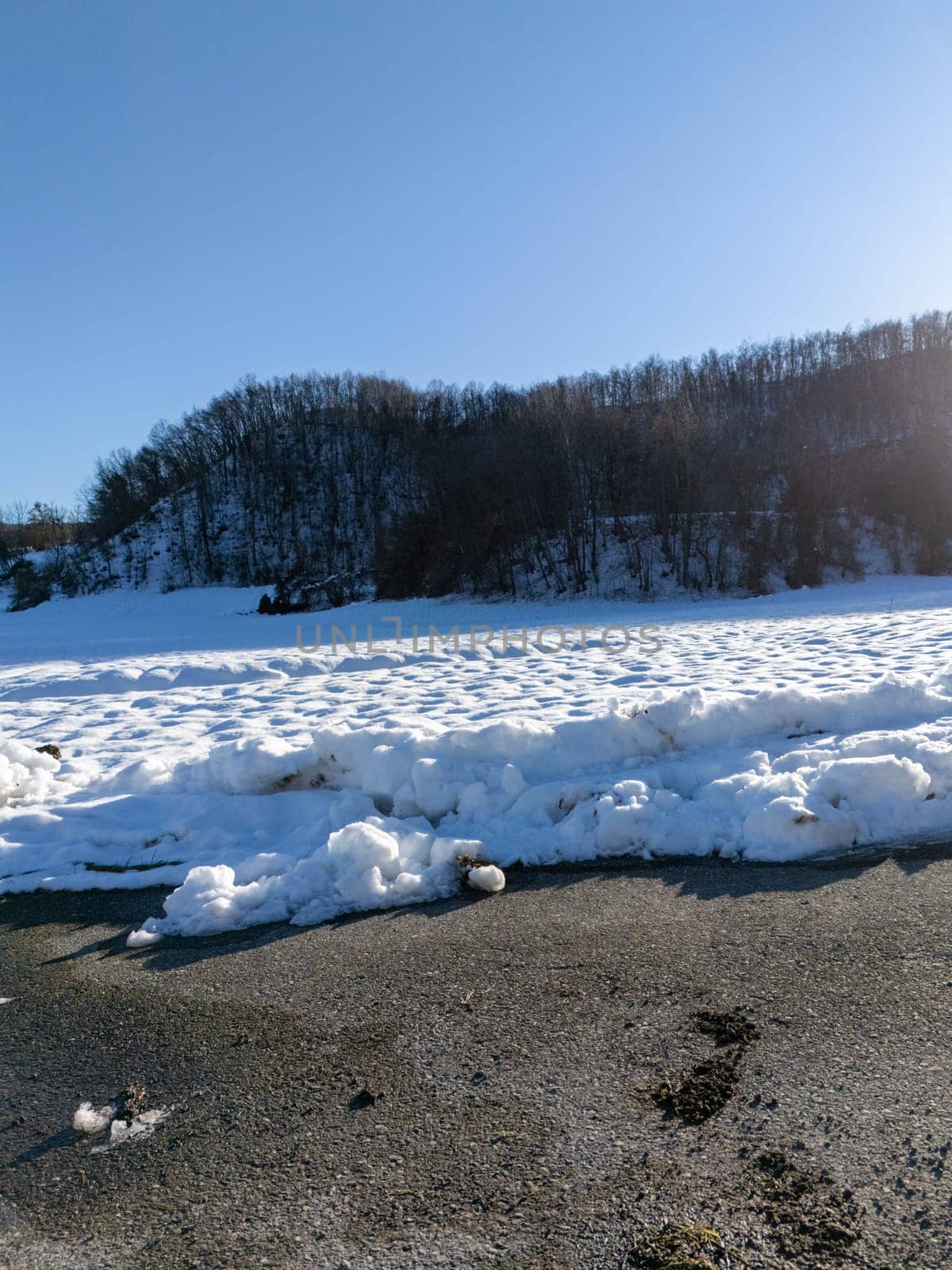 Snow covering the landscape of Monte Lama in Morfasso, Italy, during the winter season, creating a serene and picturesque scene with a clear blue sky and bare trees on the hill
