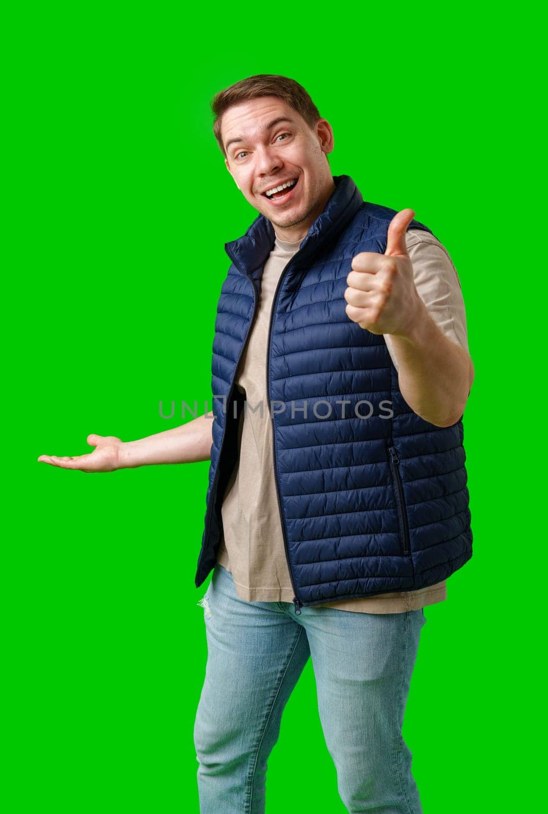 A man in a blue vest stands against a green background in studio