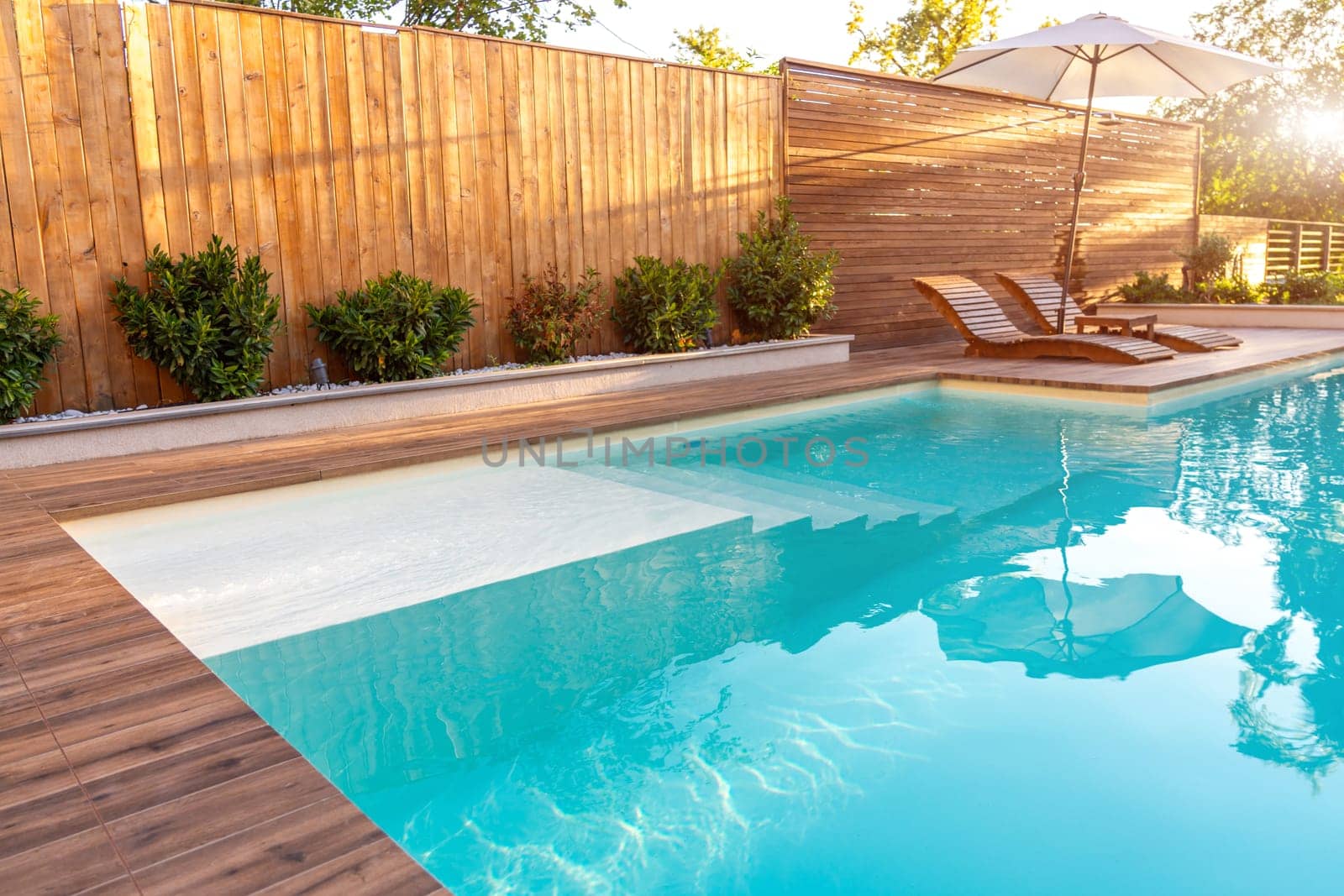 Modern backyard pool with wooden deck and sun loungers. Bright and peaceful outdoor relaxation area with natural sunlight