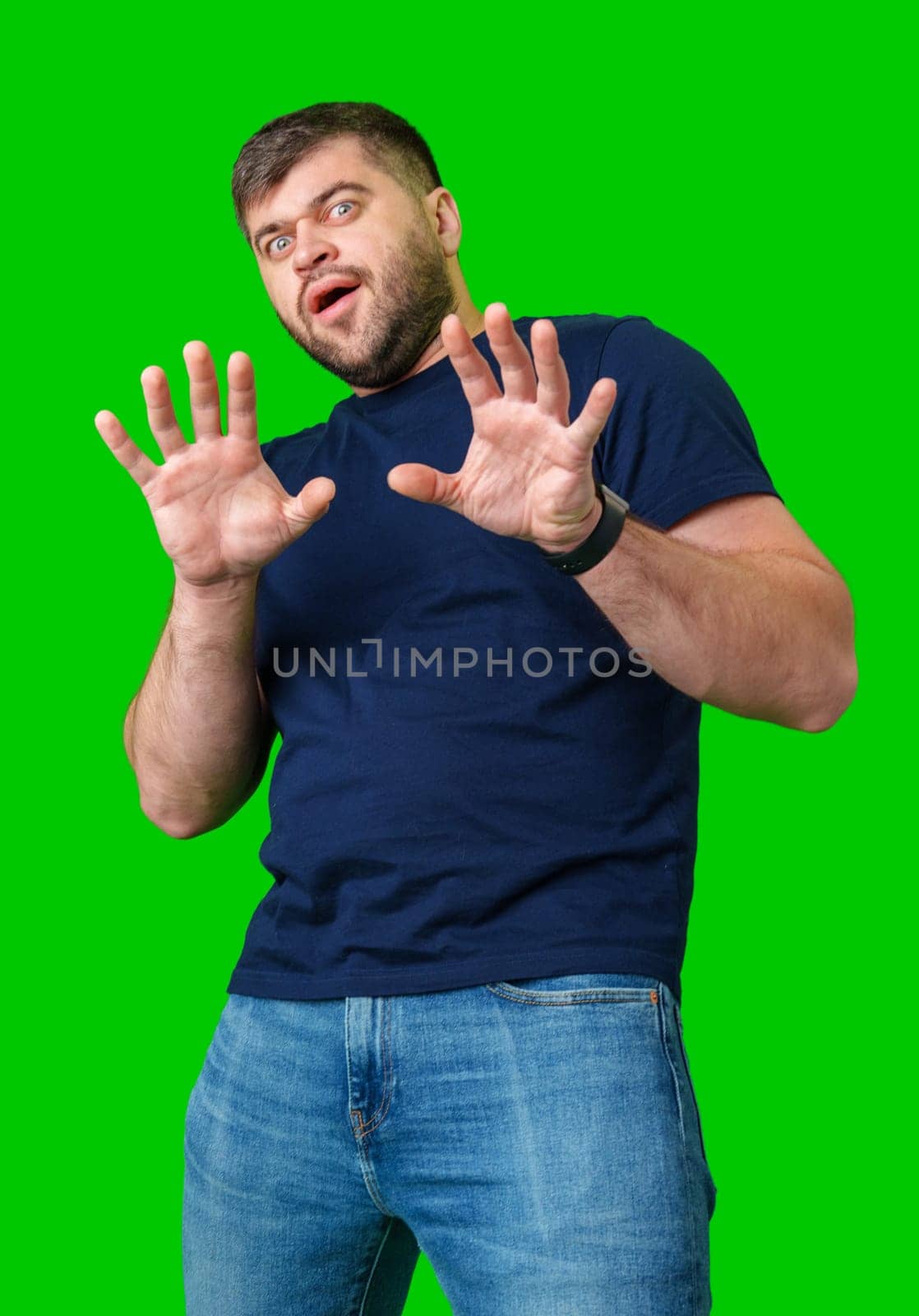 A man with a serious expression holds up both hands in a stopping gesture against a bright green background in studio