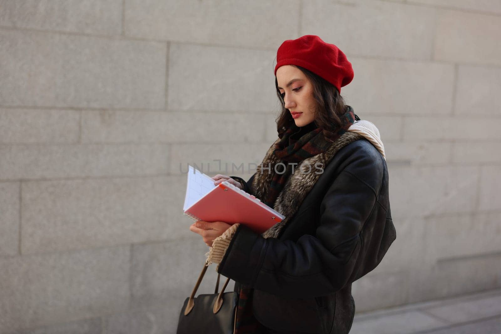 A stylish woman in a red beret jots down ideas while walking, highlighting her urban fashion and creativity