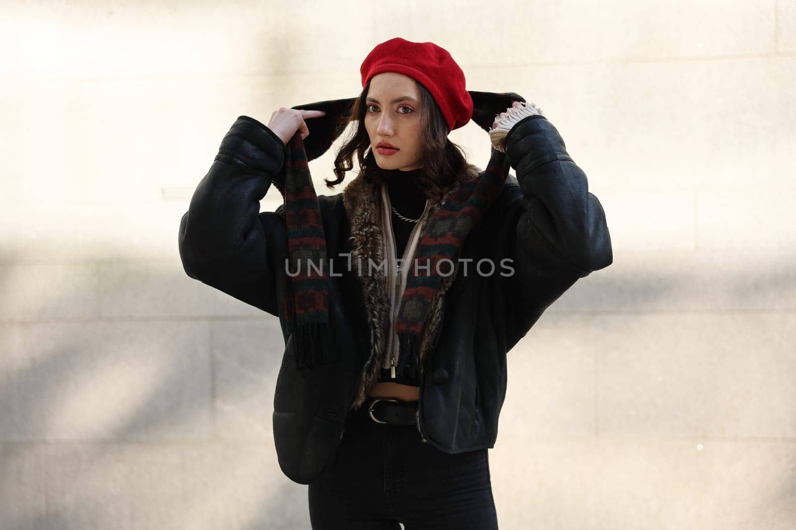 A woman exuding effortless style, donning a striking red beret, poses elegantly against an interesting, textured wall