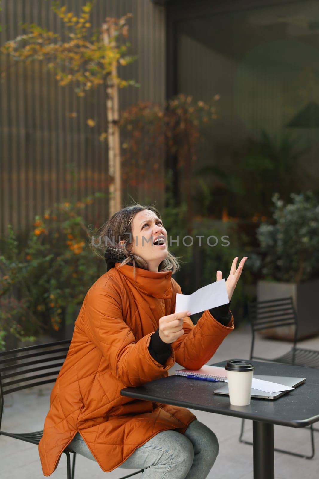 A woman expresses frustration while reading a document at an outdoor caf setting