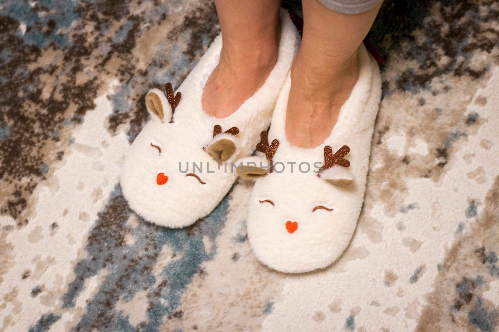 Woman wearing funny, deer shaped, soft christmas shoes. Playfully moves them in front of christmas tree.