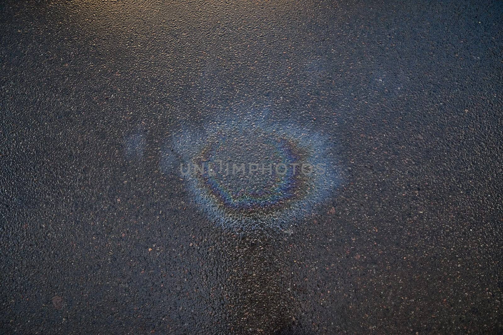Iridescent gasoline spill forming a colorful circle on a wet asphalt surface