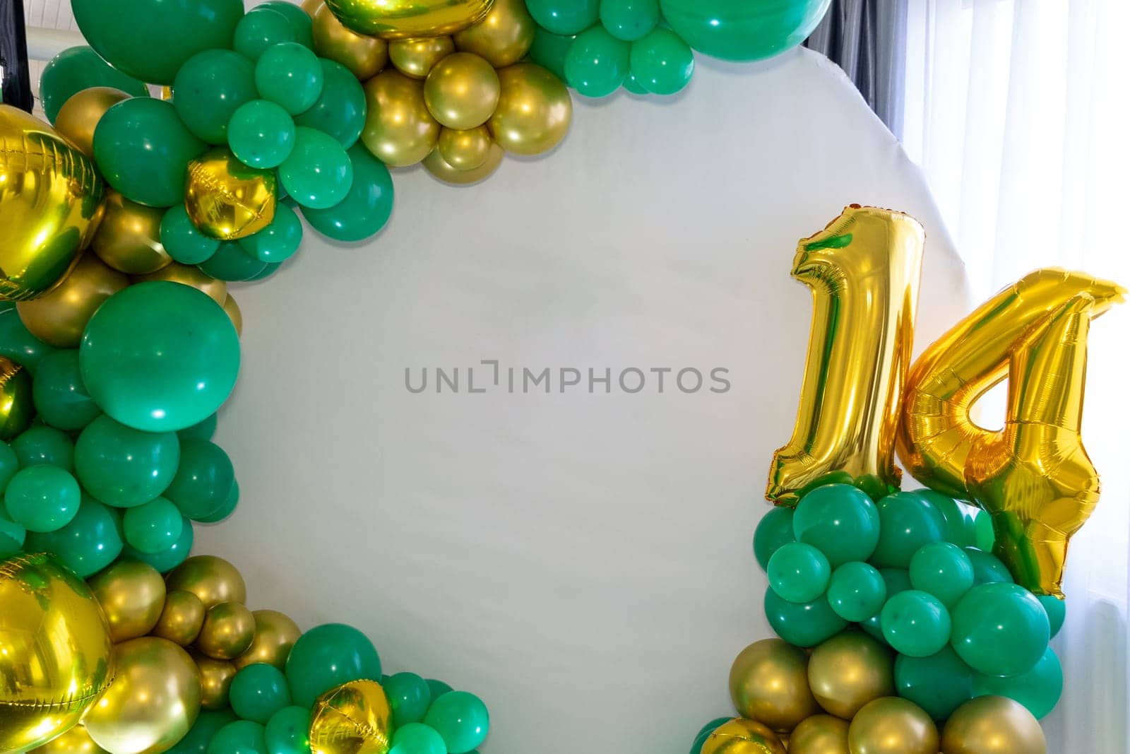 A vibrant balloon arch features green and gold hues, highlighting the number 14, perfect for a birthday celebration. The setup exudes a joyful atmosphere for the special occasion.