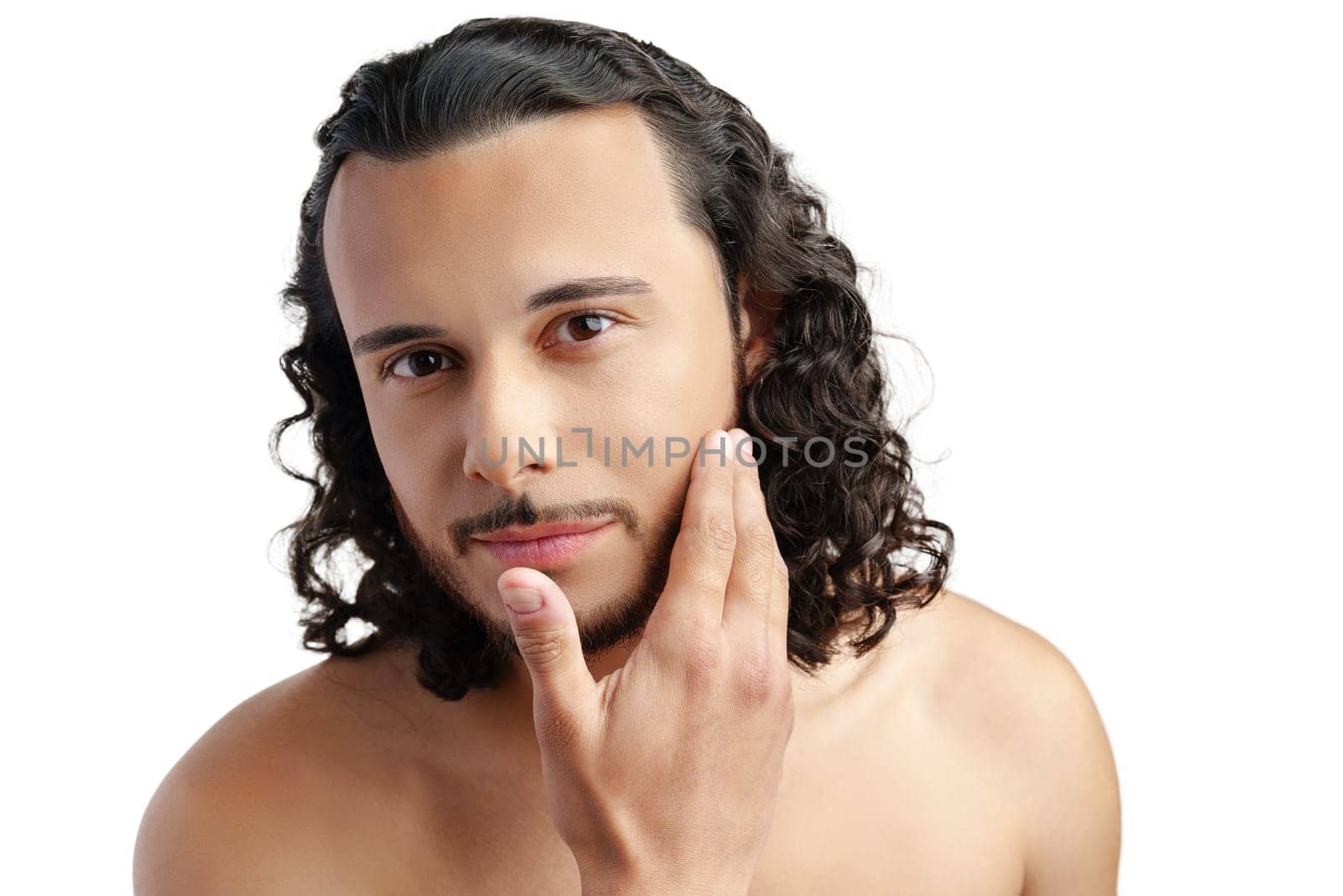 Young man with curly hair thoughtfully posing against a plain background in a studio setting
