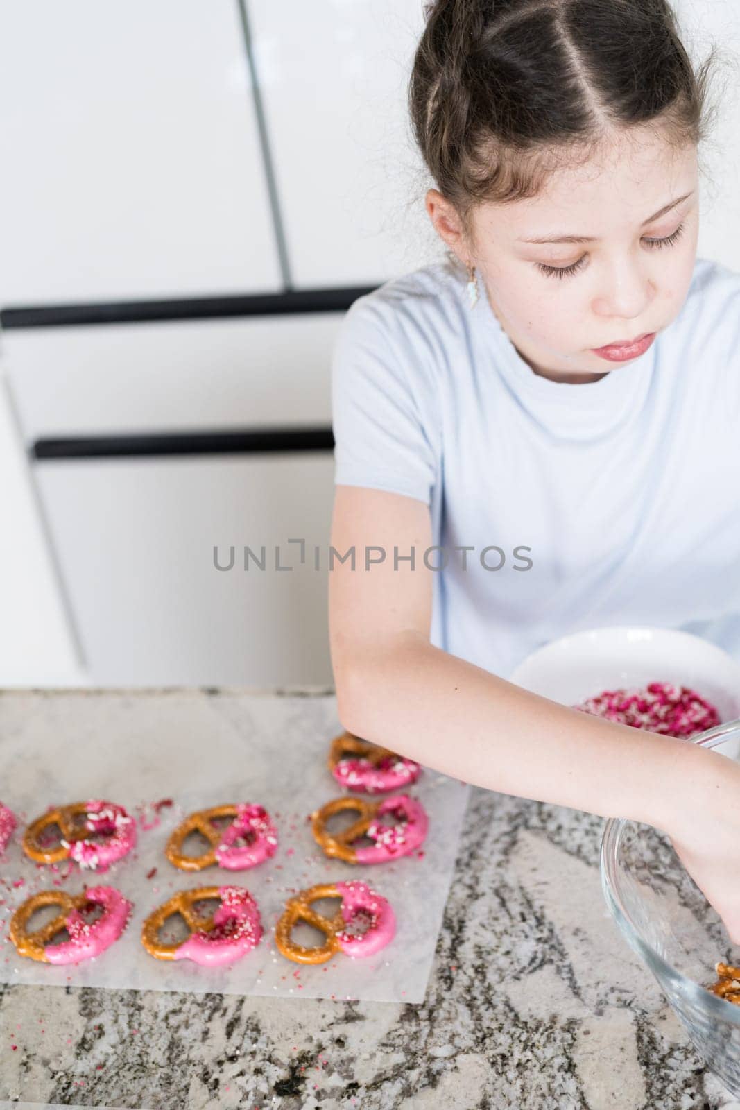 With focused attention, this budding culinary artist dips pretzels into a pot of melted chocolate, creating sweet delights in the warmth of a well-lit home kitchen.