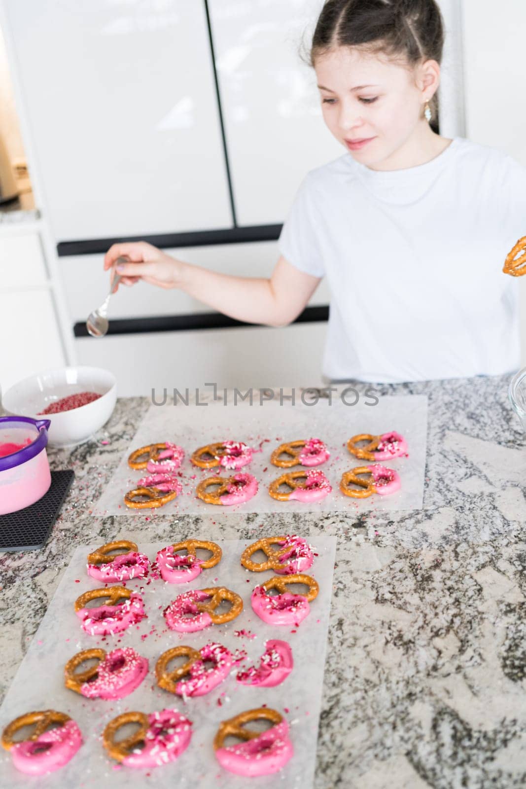 With focused attention, this budding culinary artist dips pretzels into a pot of melted chocolate, creating sweet delights in the warmth of a well-lit home kitchen.