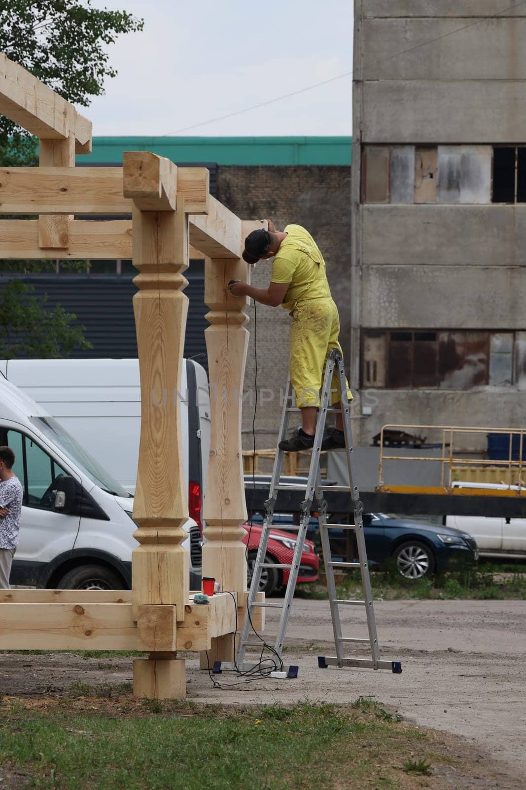 A diligent worker in yellow overalls carefully installs a sturdy wooden beam on a bustling construction site