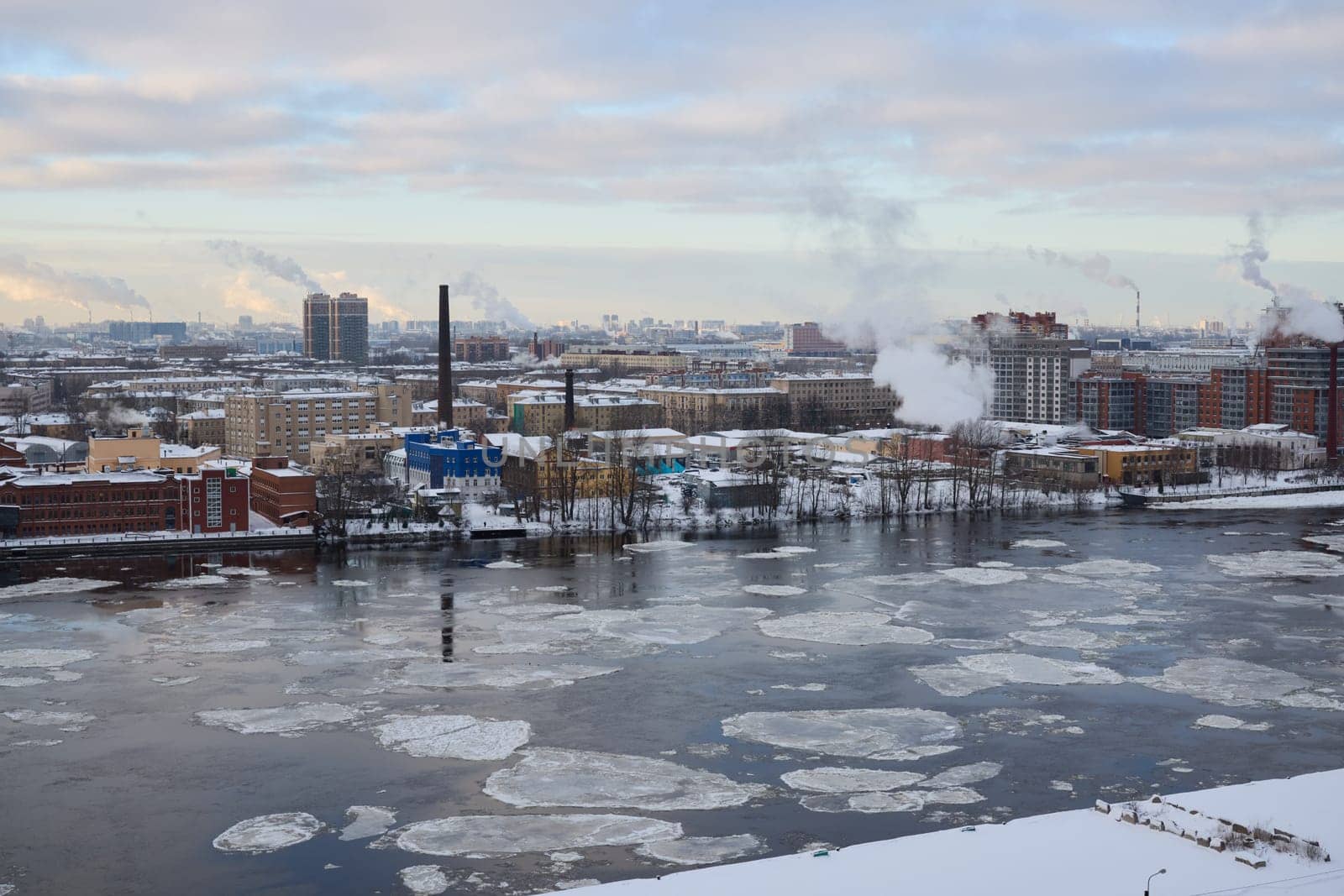 A picturesque snowy urban landscape showcasing factories, river ice formations, and serene winter scenery