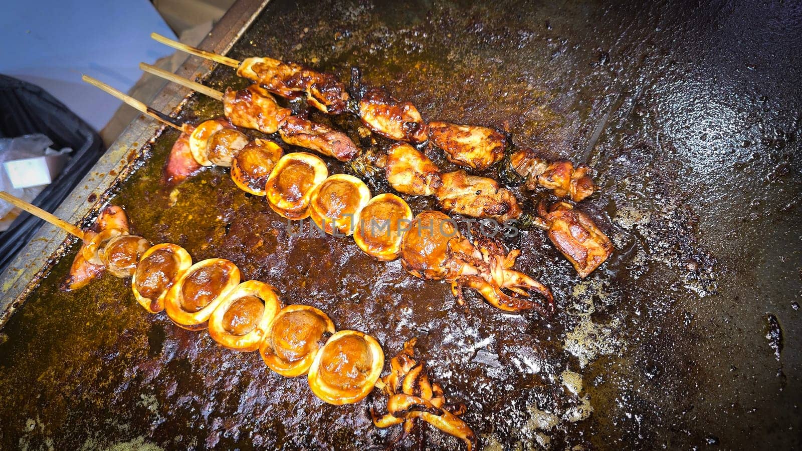 cook grills skewered squid over an open flame using a blowtorch, capturing the lively atmosphere of a bustling street food Thai market with bright flames and freshly prepared seafood.