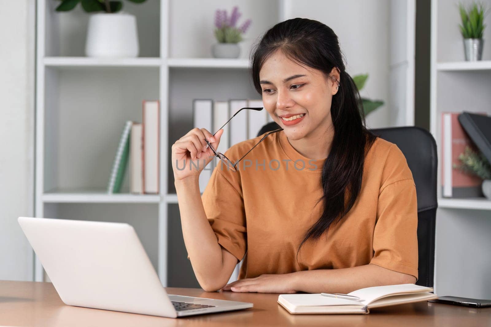 Young woman studying online at home, using a laptop and notebook, engaged in e-learning and remote education.