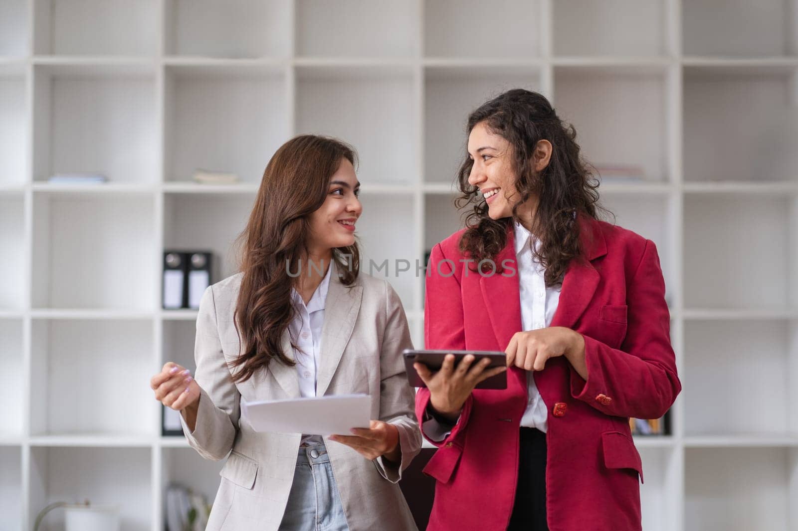 Two businesswomen engage in a collaborative discussion with colleagues, showcasing teamwork and professional consultation in a modern office setting.