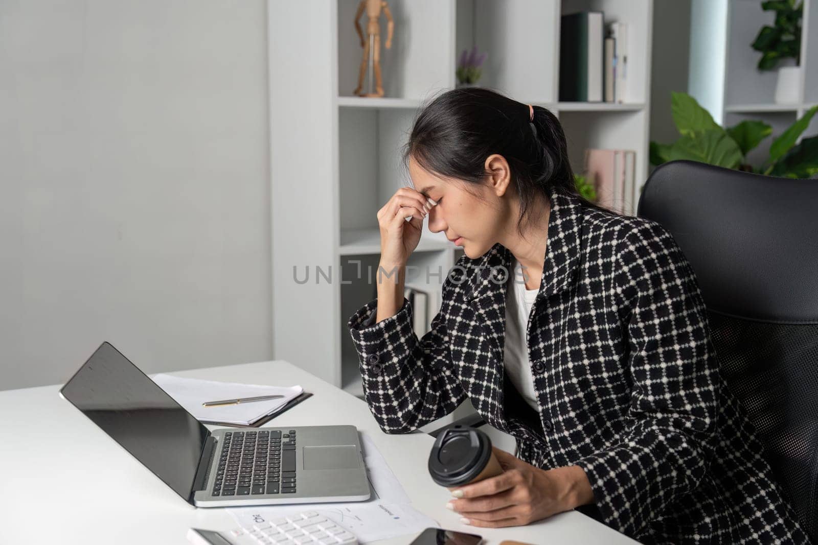 A young accountant experiencing stress while working at a desk with a laptop and coffee in a modern office setting.