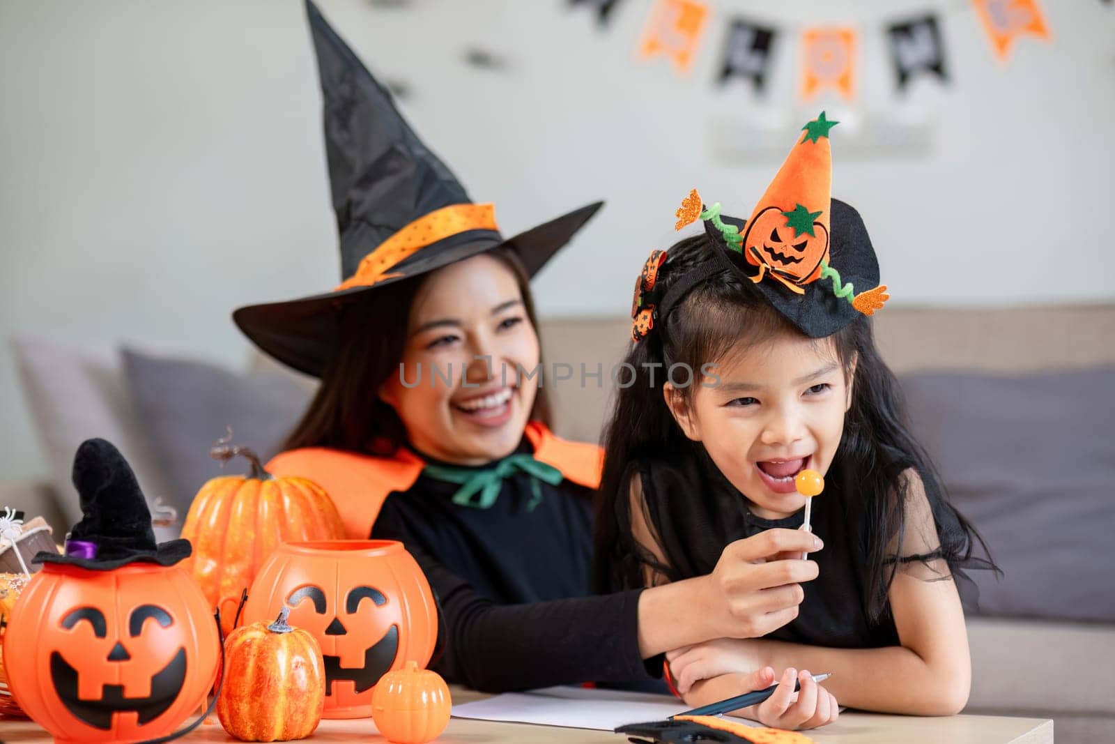 A mother and child dressed as witches engage in Halloween activities, surrounded by festive pumpkins and decorations, creating joyful holiday memories.