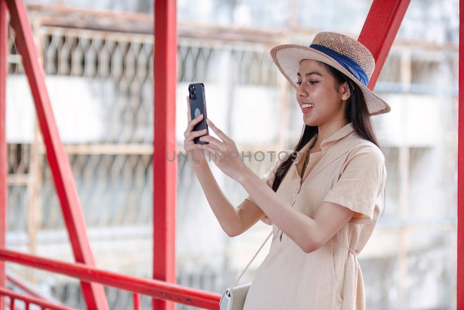 A young female tourist in a summer dress and hat uses her mobile phone to explore and capture memories at a city tourist attraction.