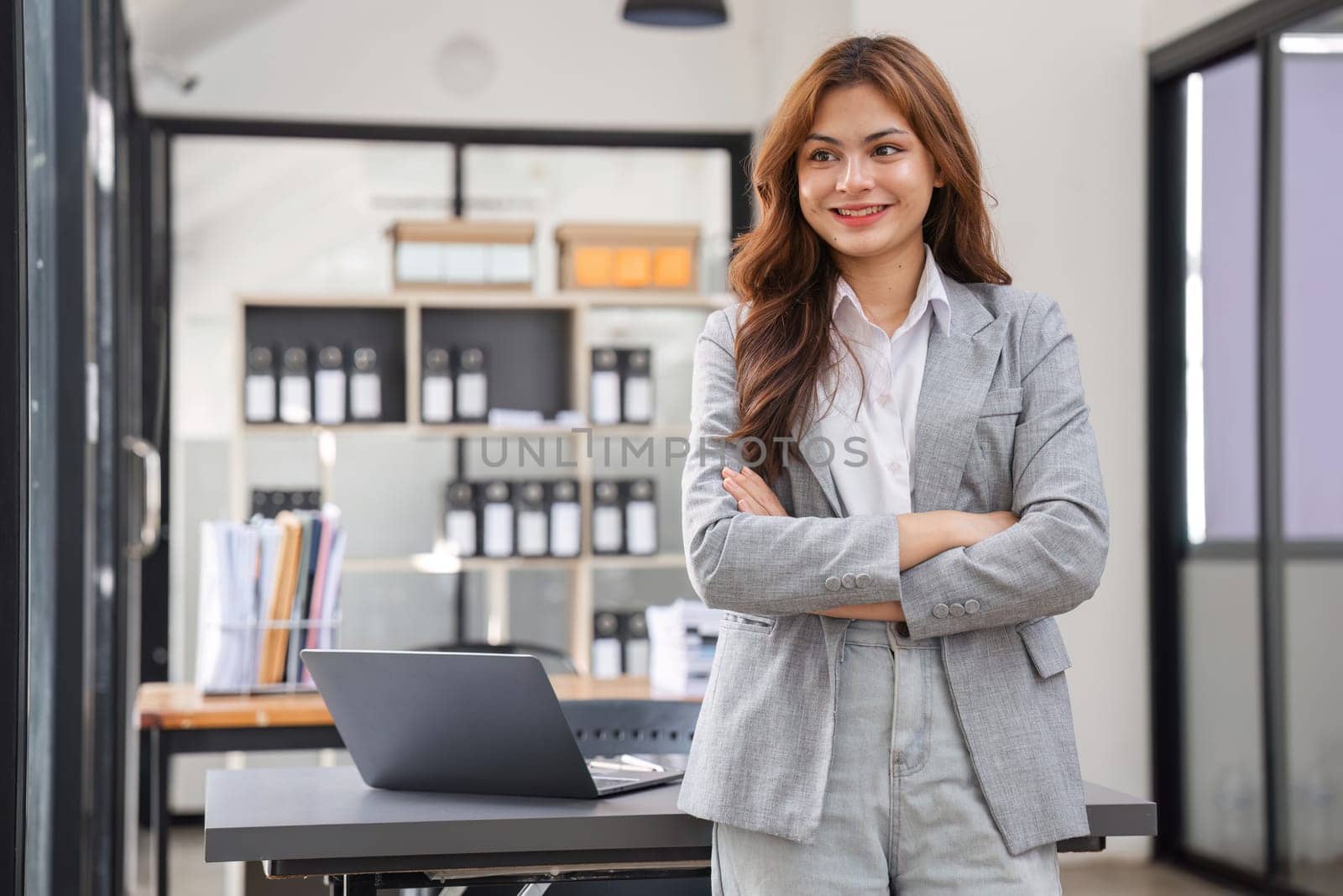 A confident young businesswoman stands at her desk, exuding professionalism in a modern office environment.