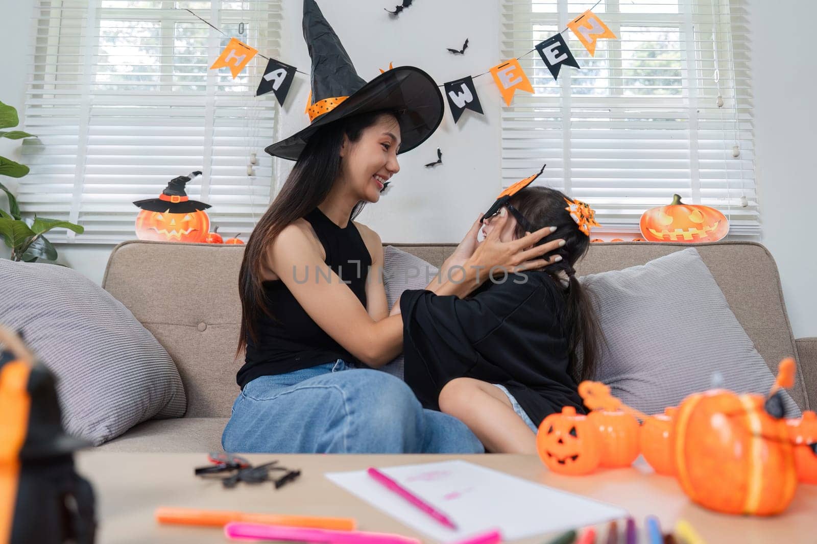 A mother and daughter share a joyful moment on Halloween, dressed in costumes and surrounded by festive decorations.