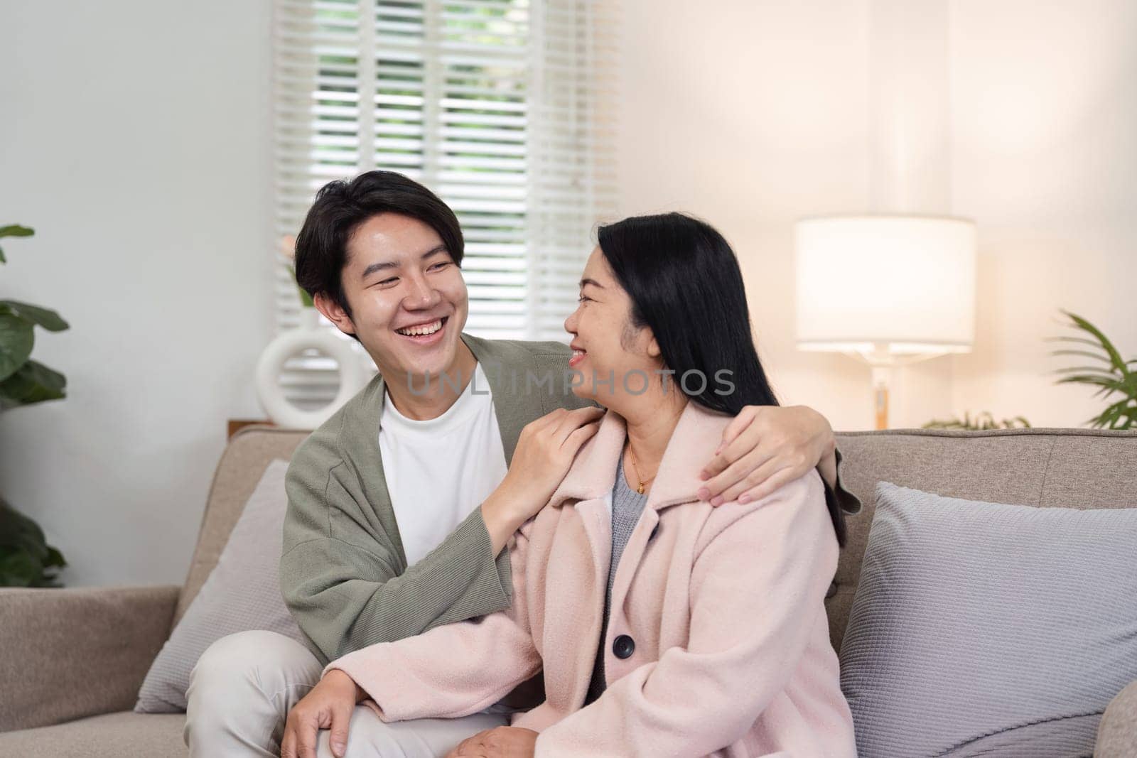A mother and her son are sitting together on a couch, smiling and enjoying each other's company during a holiday at home.