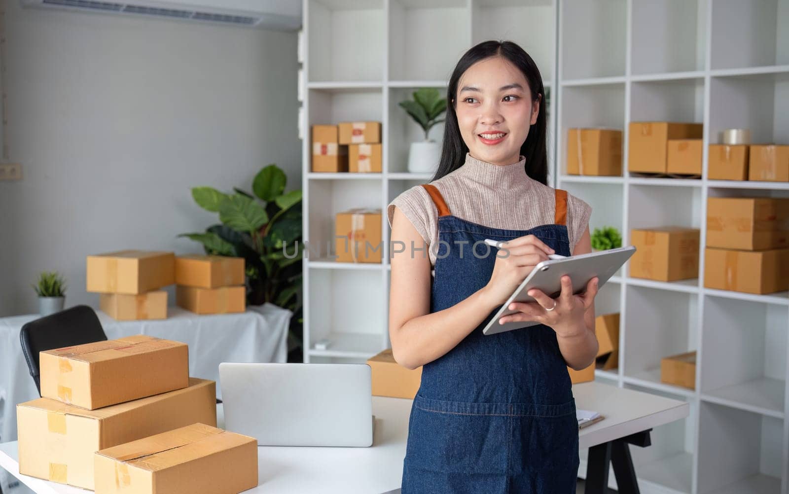 A female business owner working in her home office, managing her online selling business with packaging boxes and a digital tablet.