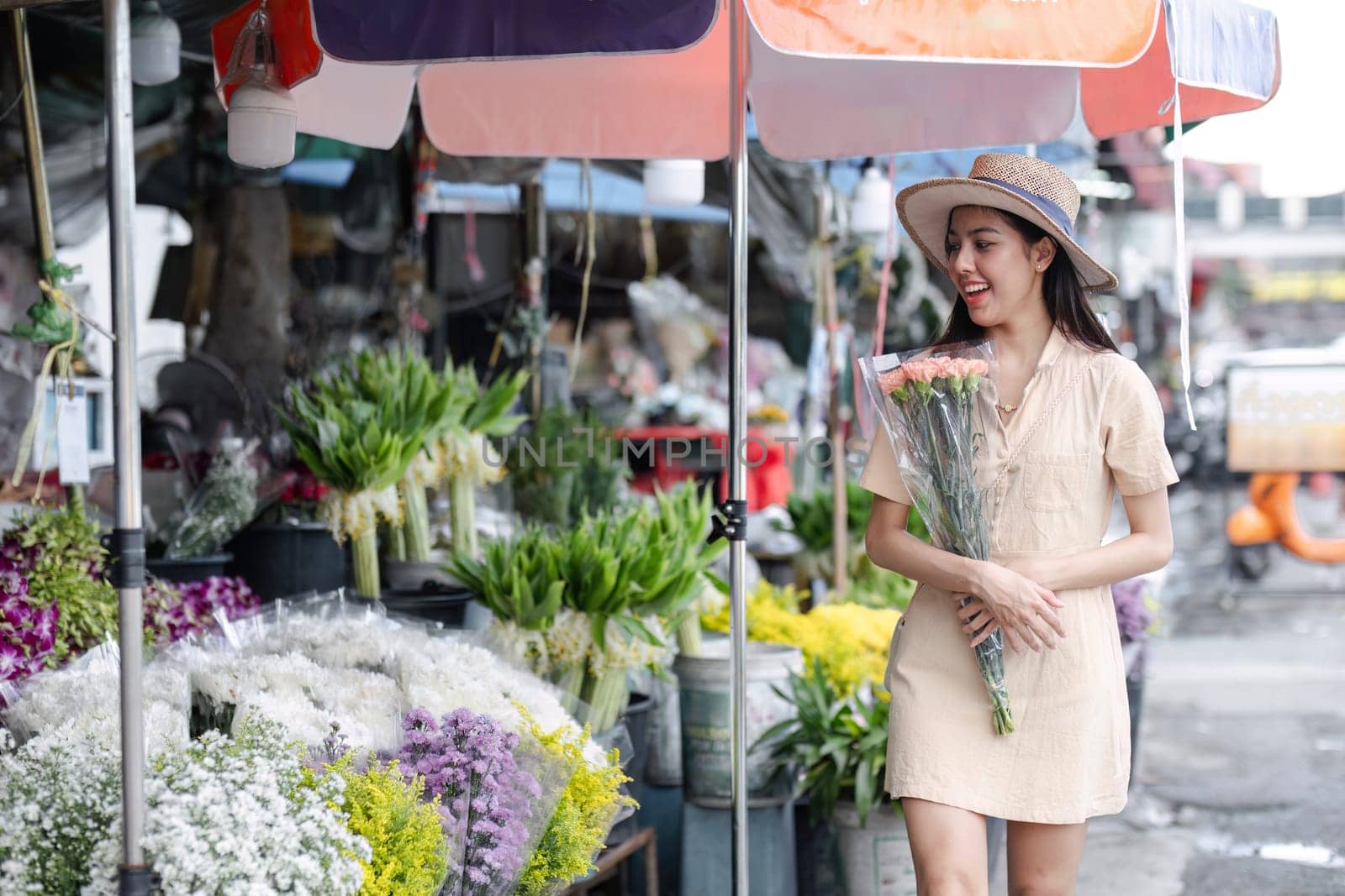 A young woman enjoys sightseeing in a bustling city market, holding a bouquet of flowers and smiling under colorful umbrellas.