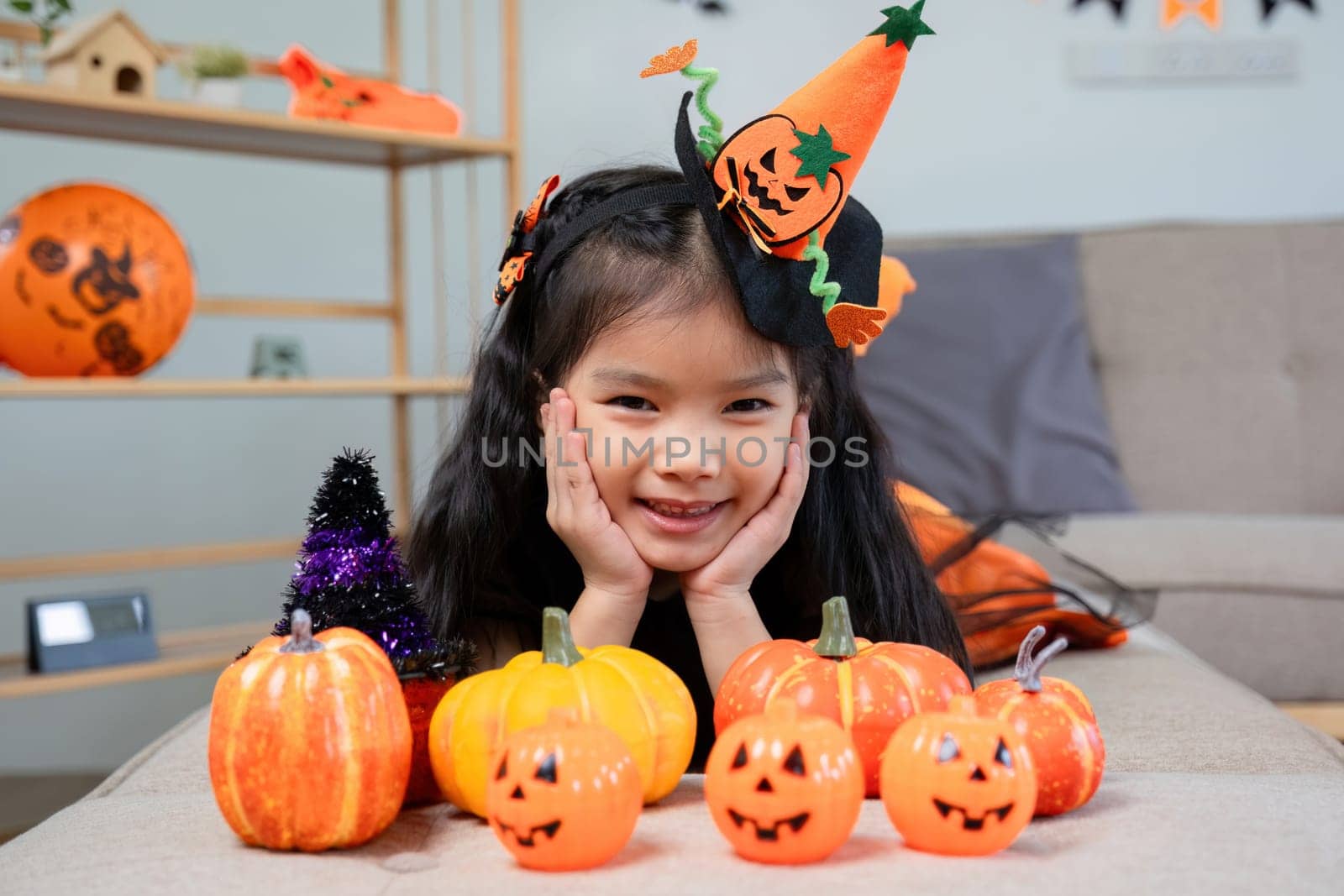 Cute girl in a Halloween costume surrounded by festive pumpkin decorations, ideal for holiday-themed stock photography.