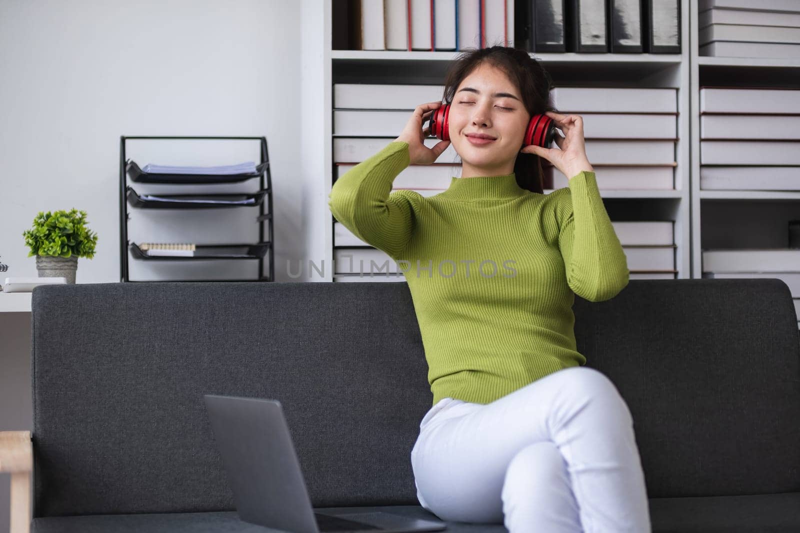Asian woman relaxing with headphones in modern office, concept of relaxation.