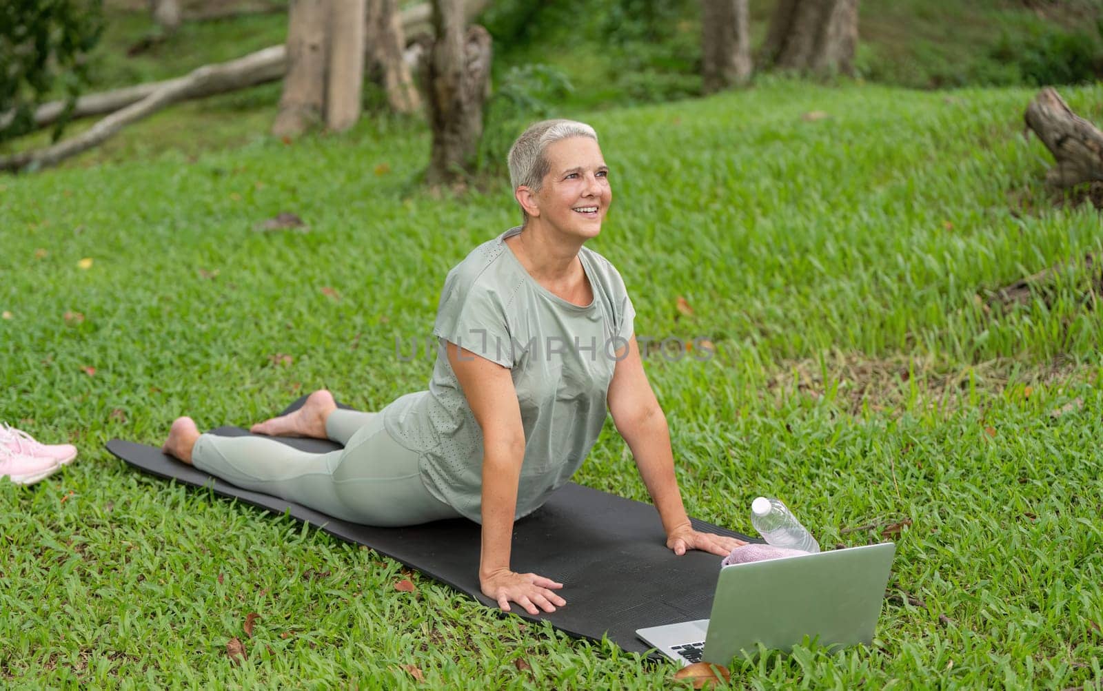 Elderly woman practicing yoga and stretching in a garden, emphasizing health, fitness, and an active lifestyle in a serene outdoor environment.
