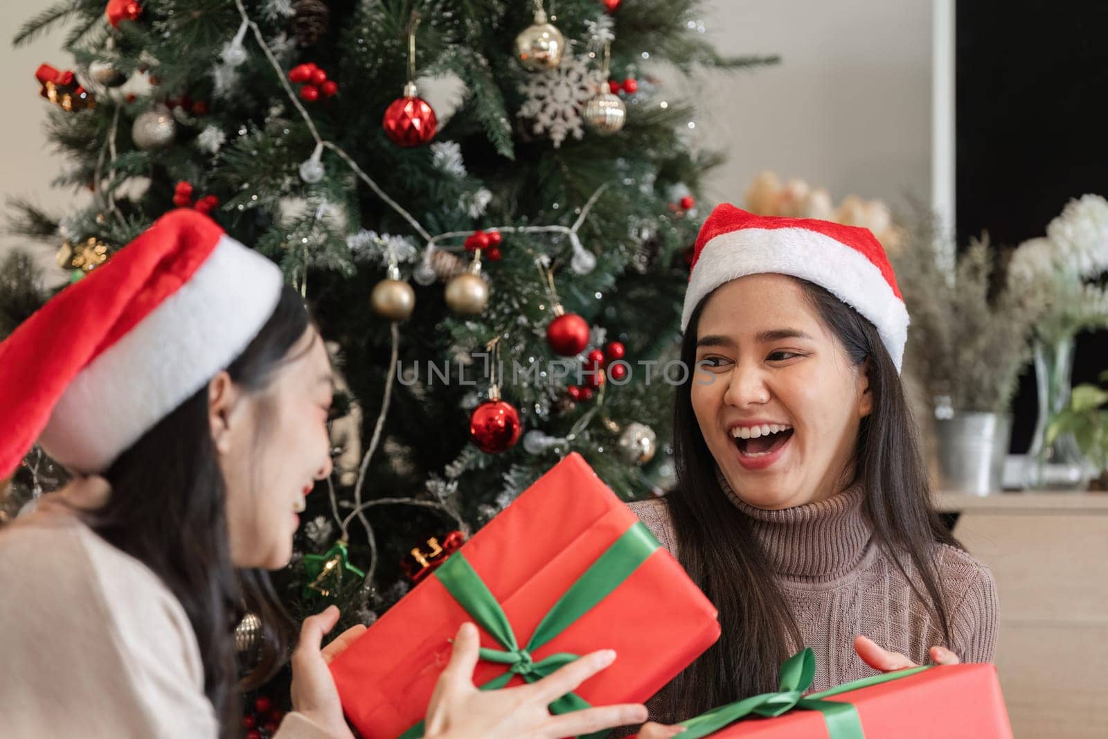 Happy young women exchanging gifts by the Christmas tree, capturing the joy and excitement of the holiday season.
