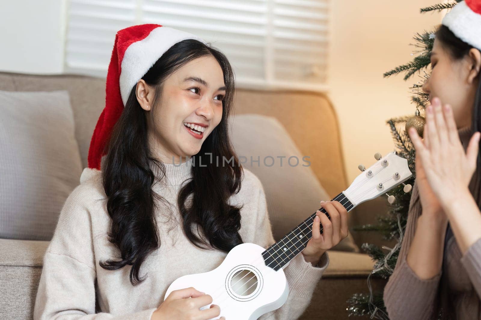 Two young women enjoying music and celebrating Christmas with joy and laughter in a cozy home environment.