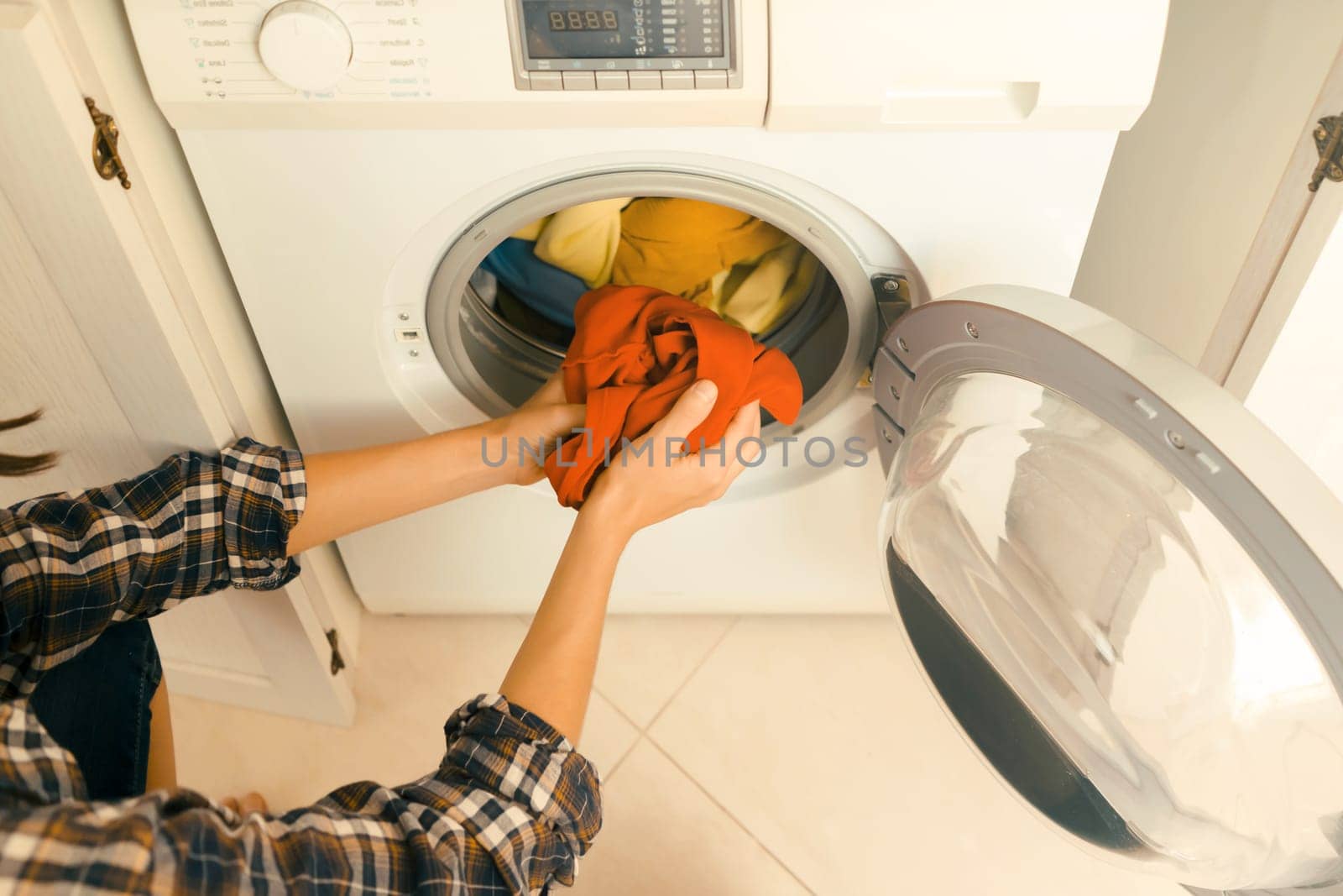 A girl folds bright clothes into a new washing machine in the bathroom at home, a woman washes things and spin them out with detergent in the laundry close-up, top view.