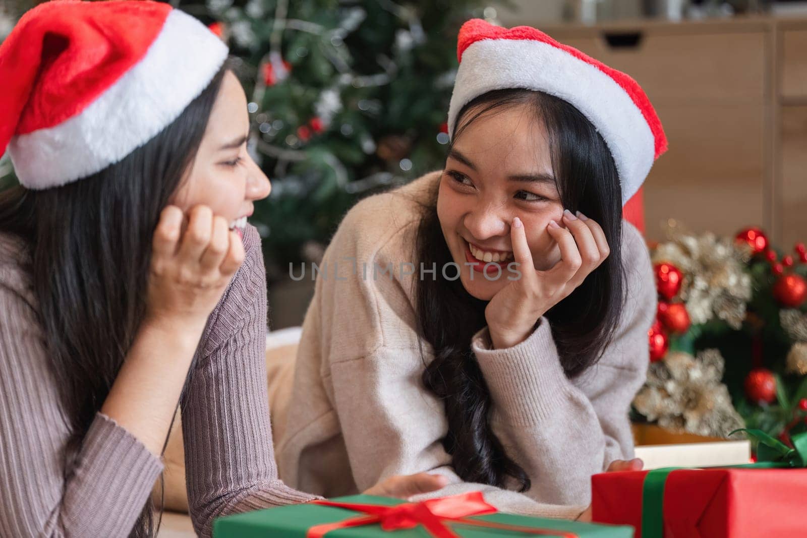 Happy lesbian couple enjoying a Christmas celebration with gifts and holiday decorations in a cozy home environment.