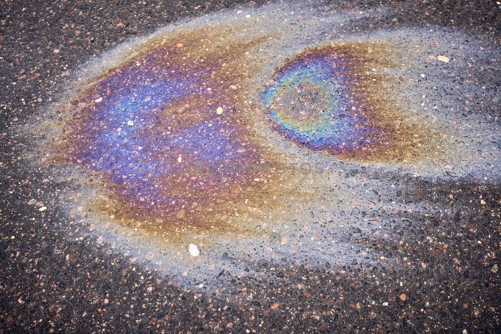 A multi-colored oil or gasoline slick that creates a bright shine on wet asphalt, illustrating the effects of environmental pollution.