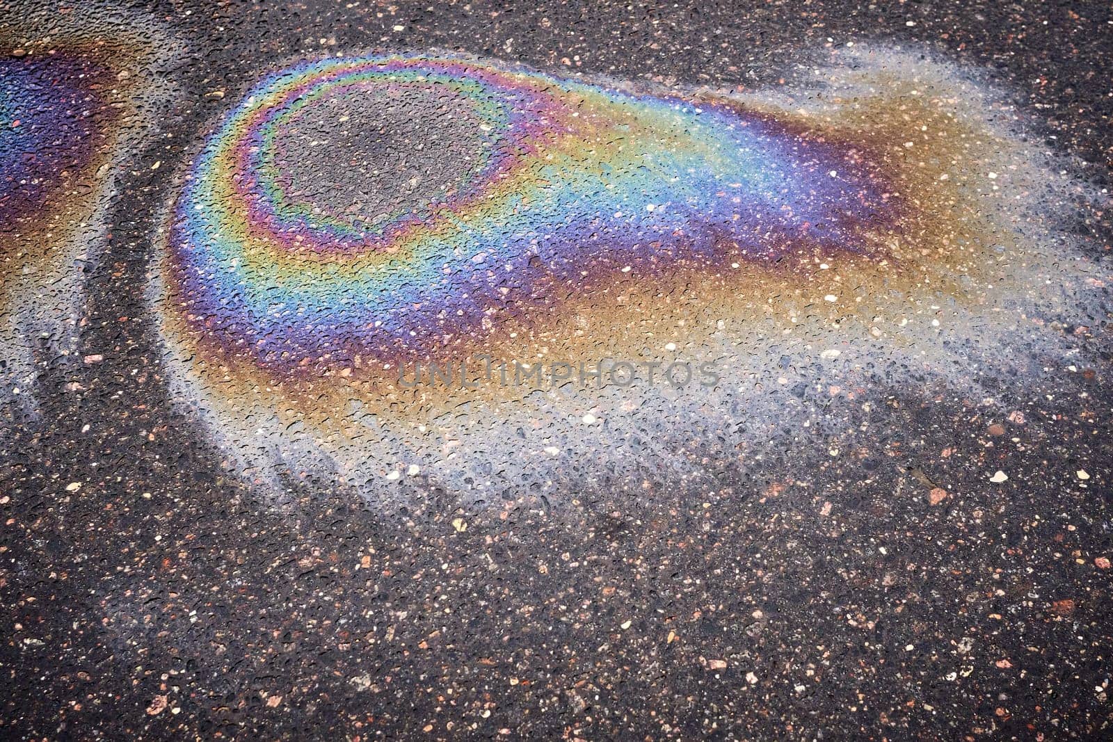 A multi-colored gasoline or oil slick creating a bright shine on wet asphalt, demonstrating environmental problems