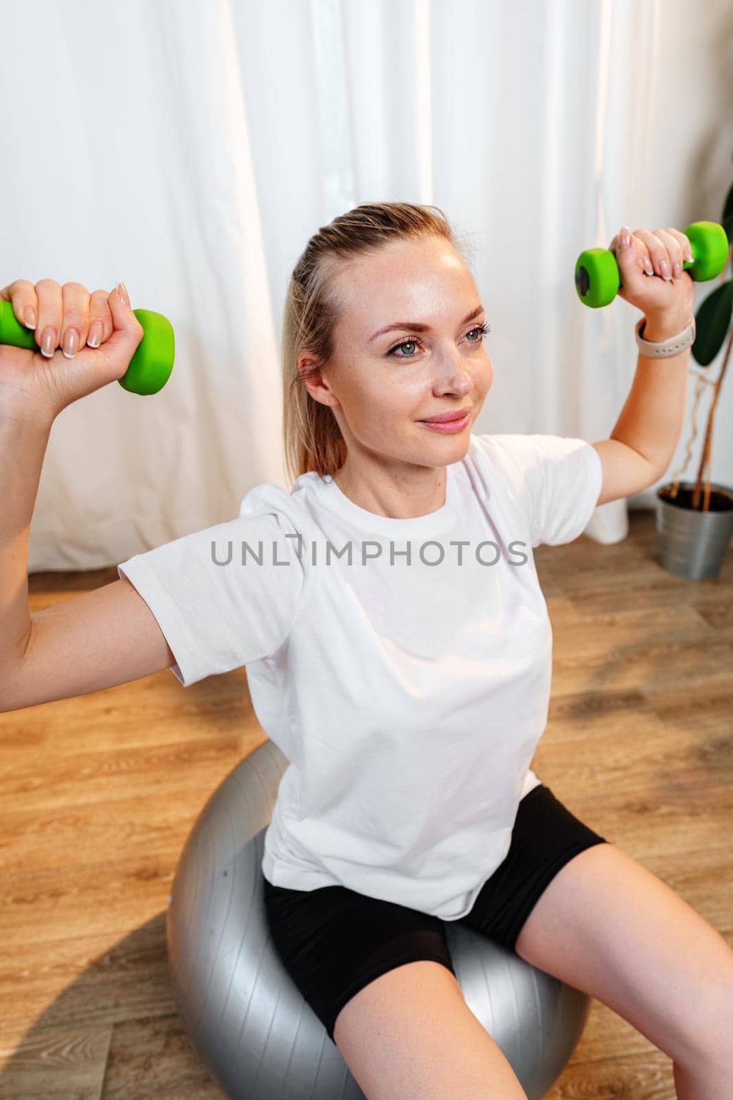 Woman exercising with dumbbells on a stability ball in a bright indoor space
