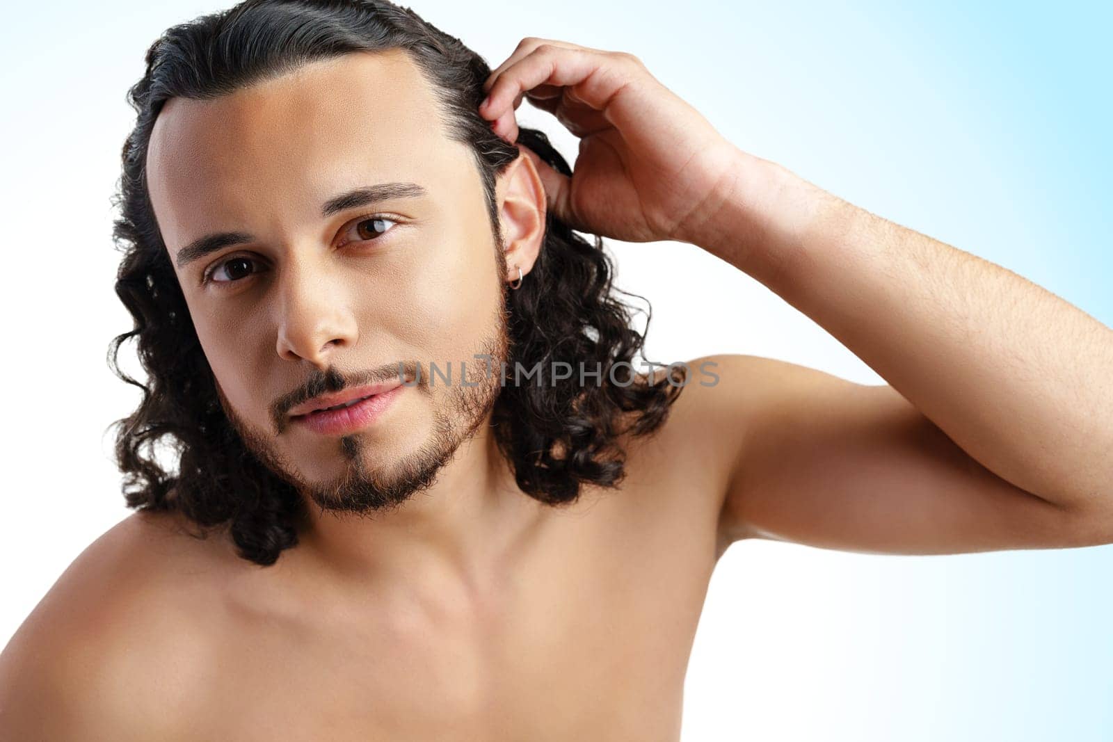Young man with curly hair thoughtfully posing against a plain background in a studio setting