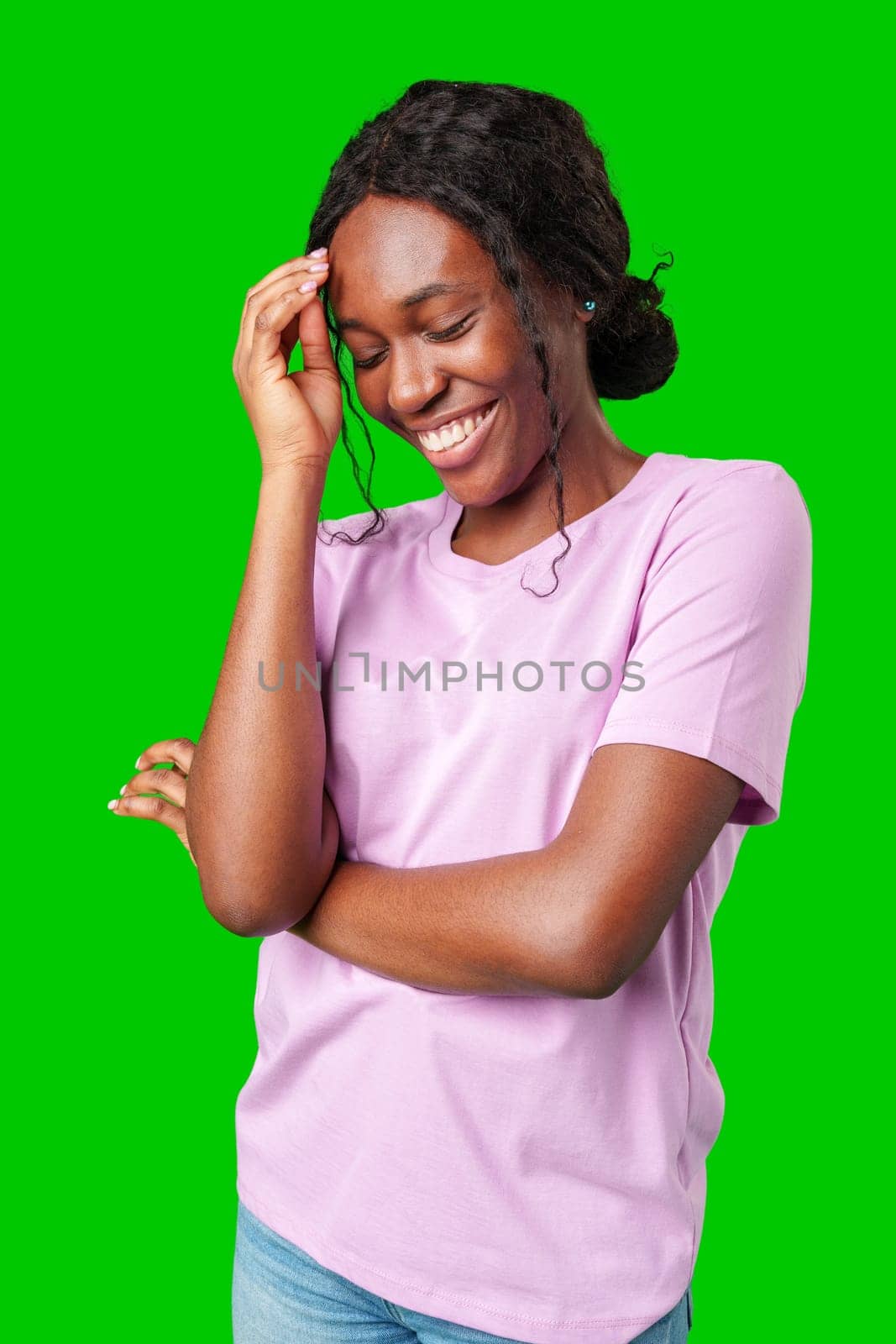 Happy young person laughing and playfully covering face while standing against a bright green background in studio