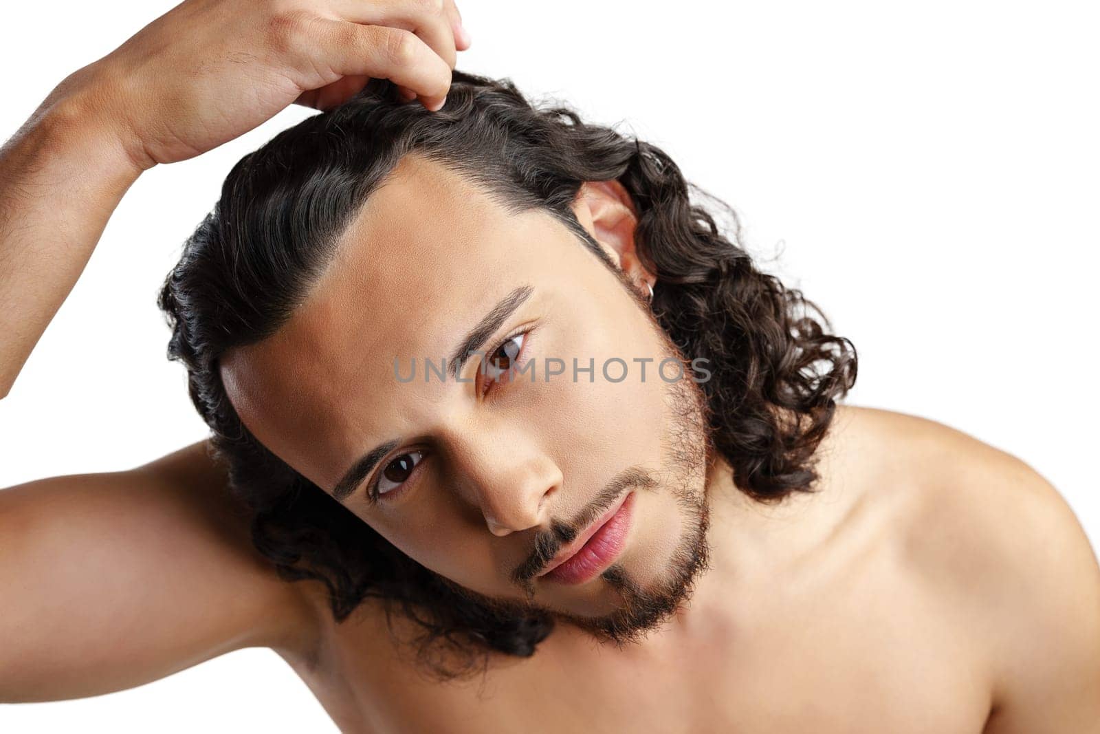 Young man with curly hair thoughtfully posing against a plain background in a studio setting