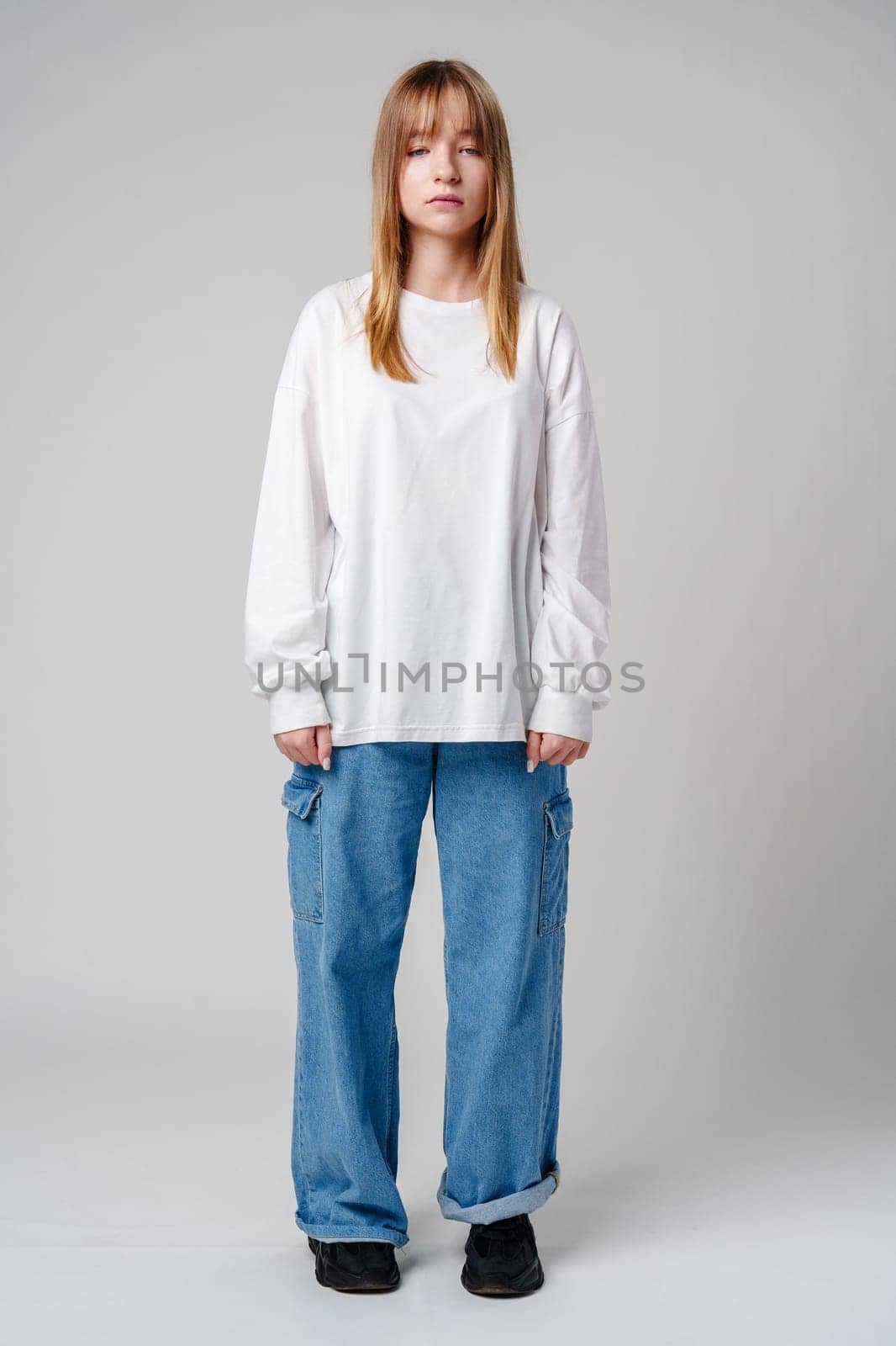 Young woman with long hair in a white sweatshirt standing against a light gray background close up