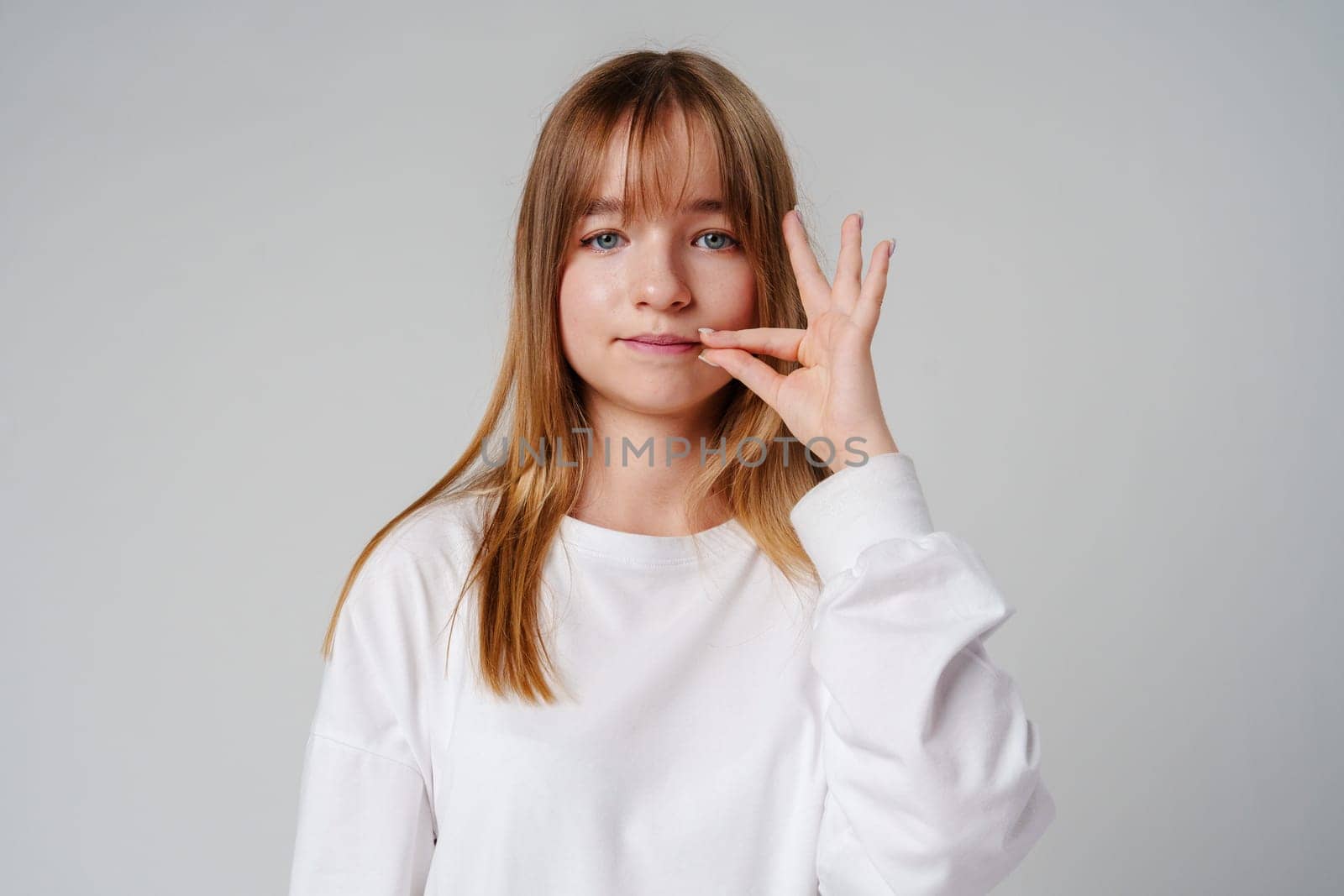 A young woman holding her finger to her lips, signaling silence in a minimalist studio setting during daylight